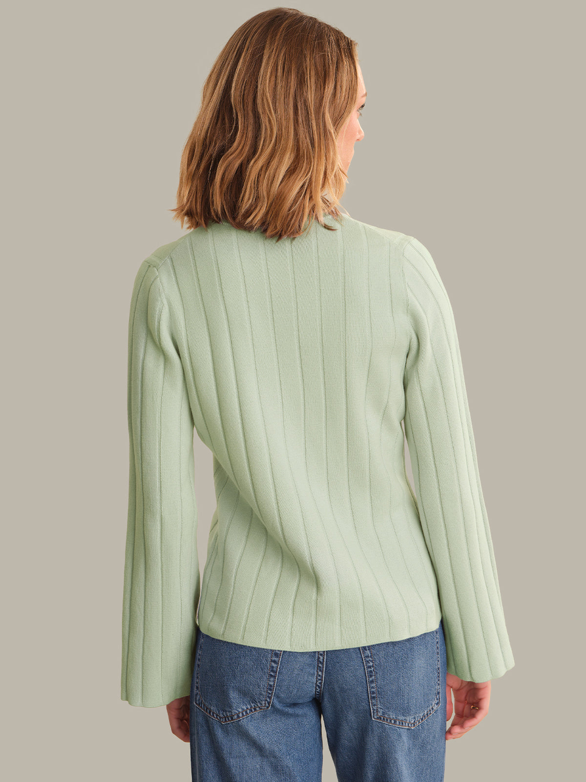Person wearing a light green ribbed cardigan and blue jeans against a plain background