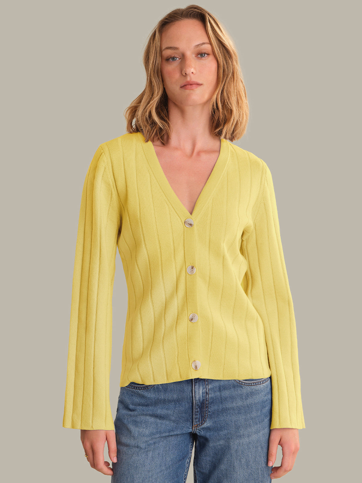 Woman wearing a yellow cardigan over a blue top against a gray background