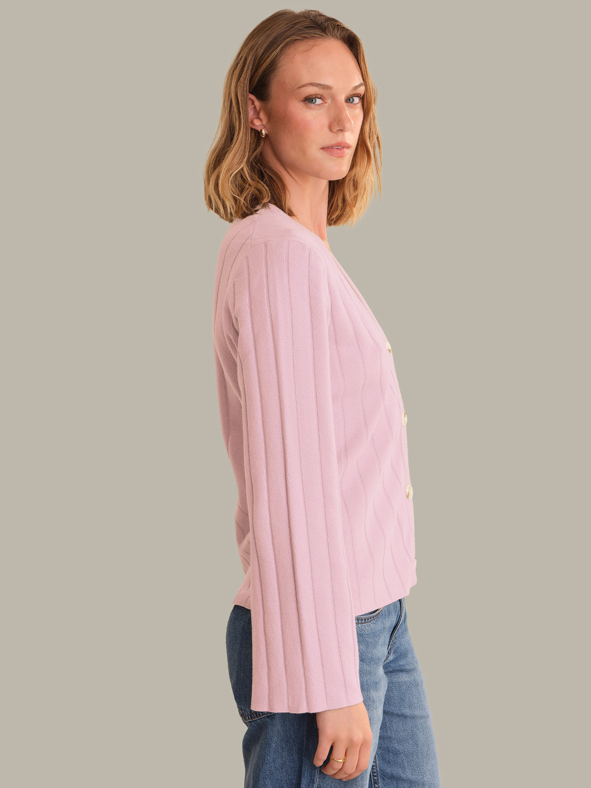 Woman wearing a pink cardigan and blue jeans against a gray background