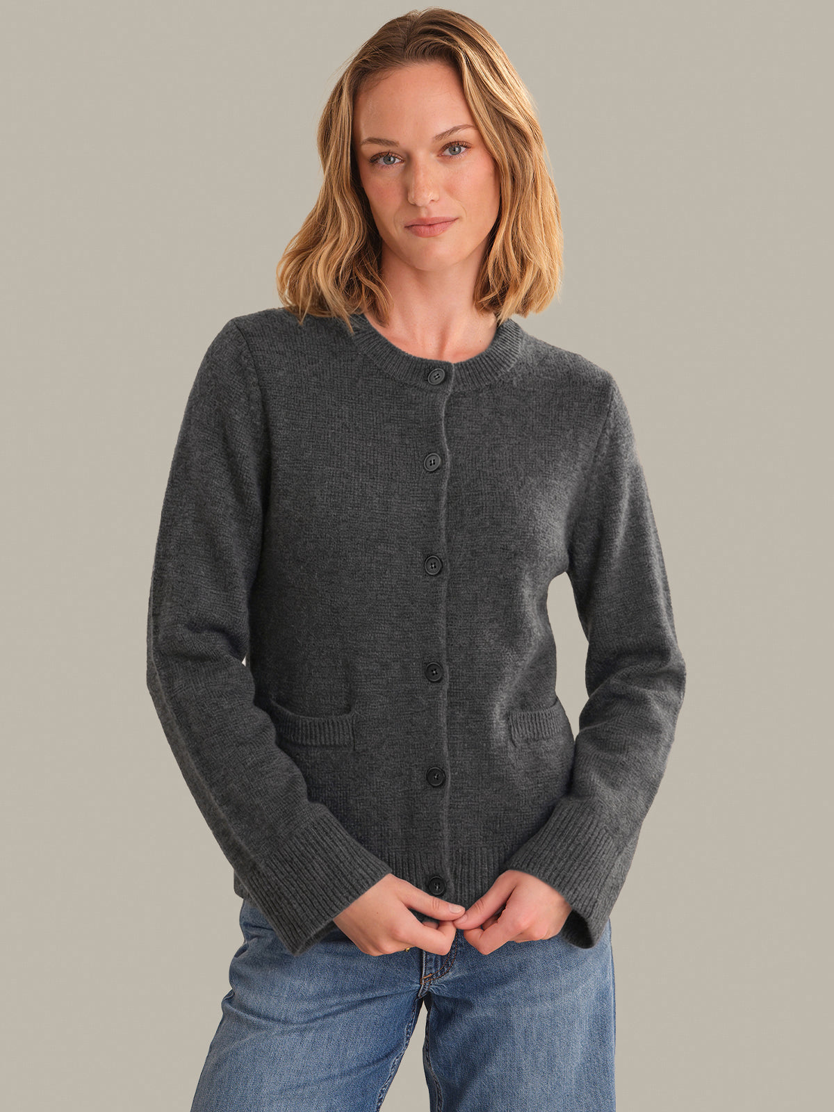 Woman wearing a dark gray cardigan over a blue shirt against a plain background