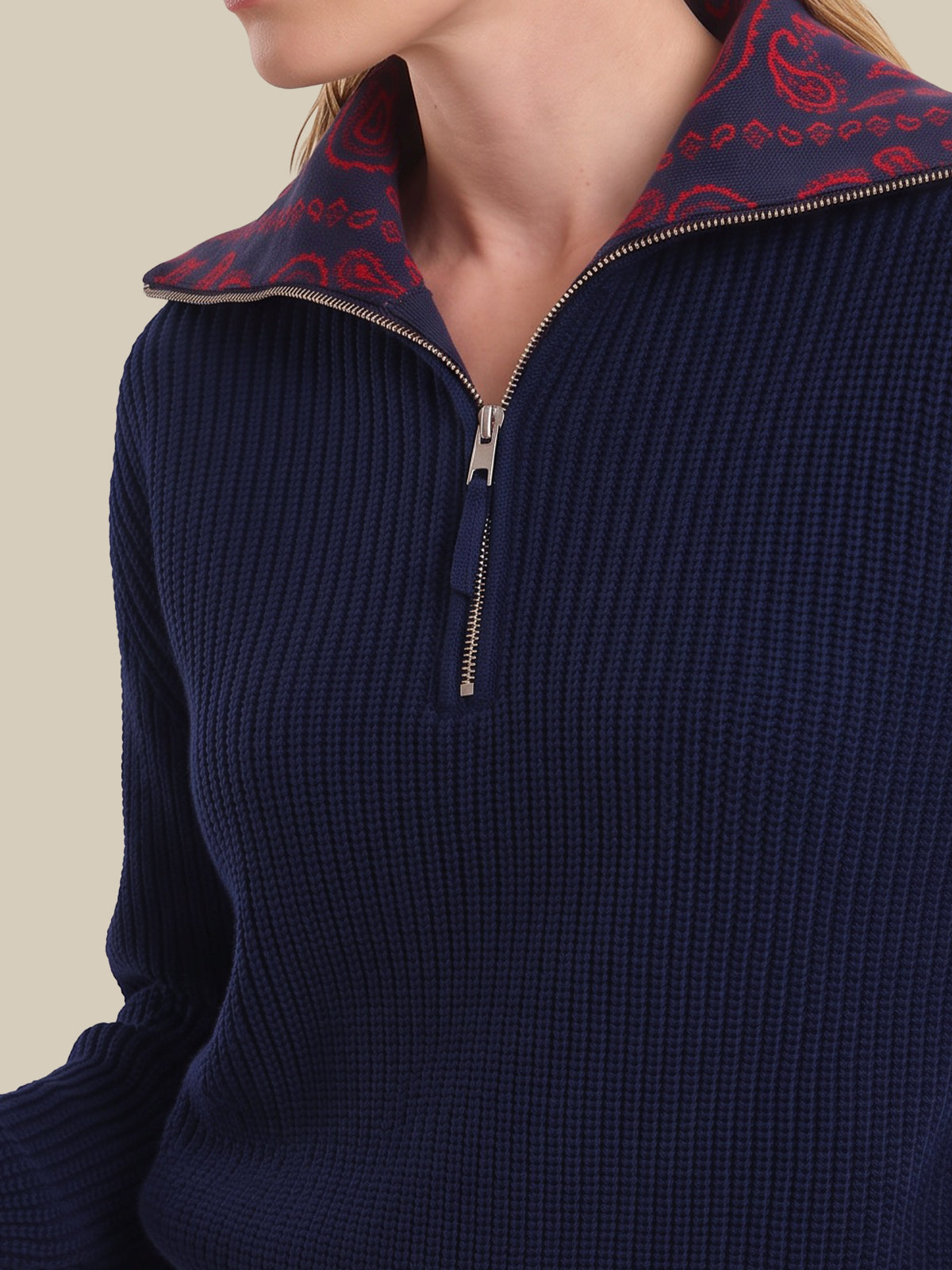 Close-up of a woman wearing a navy blue ribbed quarter-zip sweater with a red and navy paisley patterned inner collar, against a light beige background.