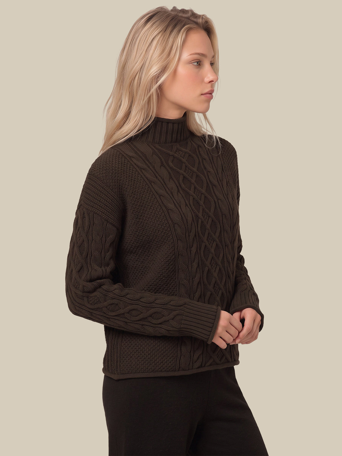 A woman wearing a dark brown cable-knit mock neck sweater, shown from a side profile against a solid beige background.