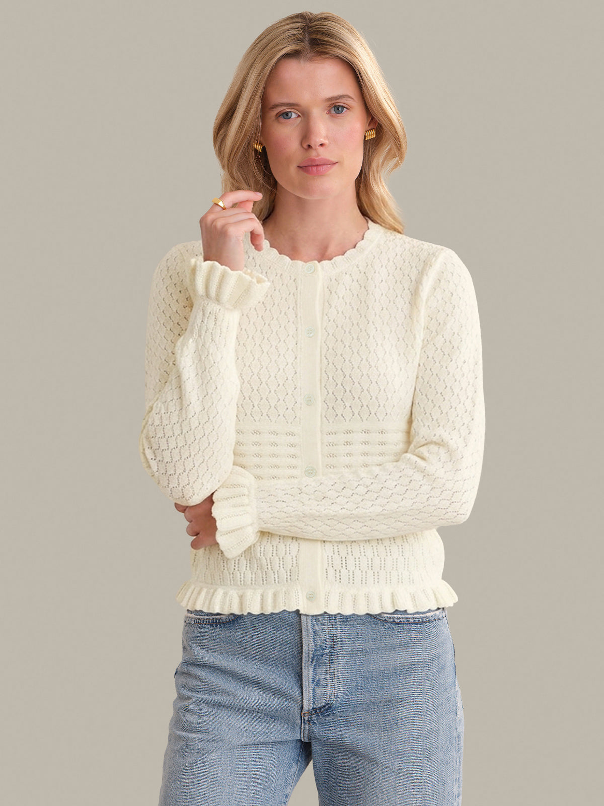 Woman wearing a cream knitted sweater and blue jeans against a plain background