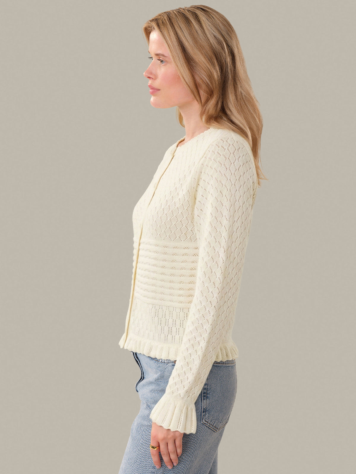 Woman wearing a cream knitted cardigan against a plain background