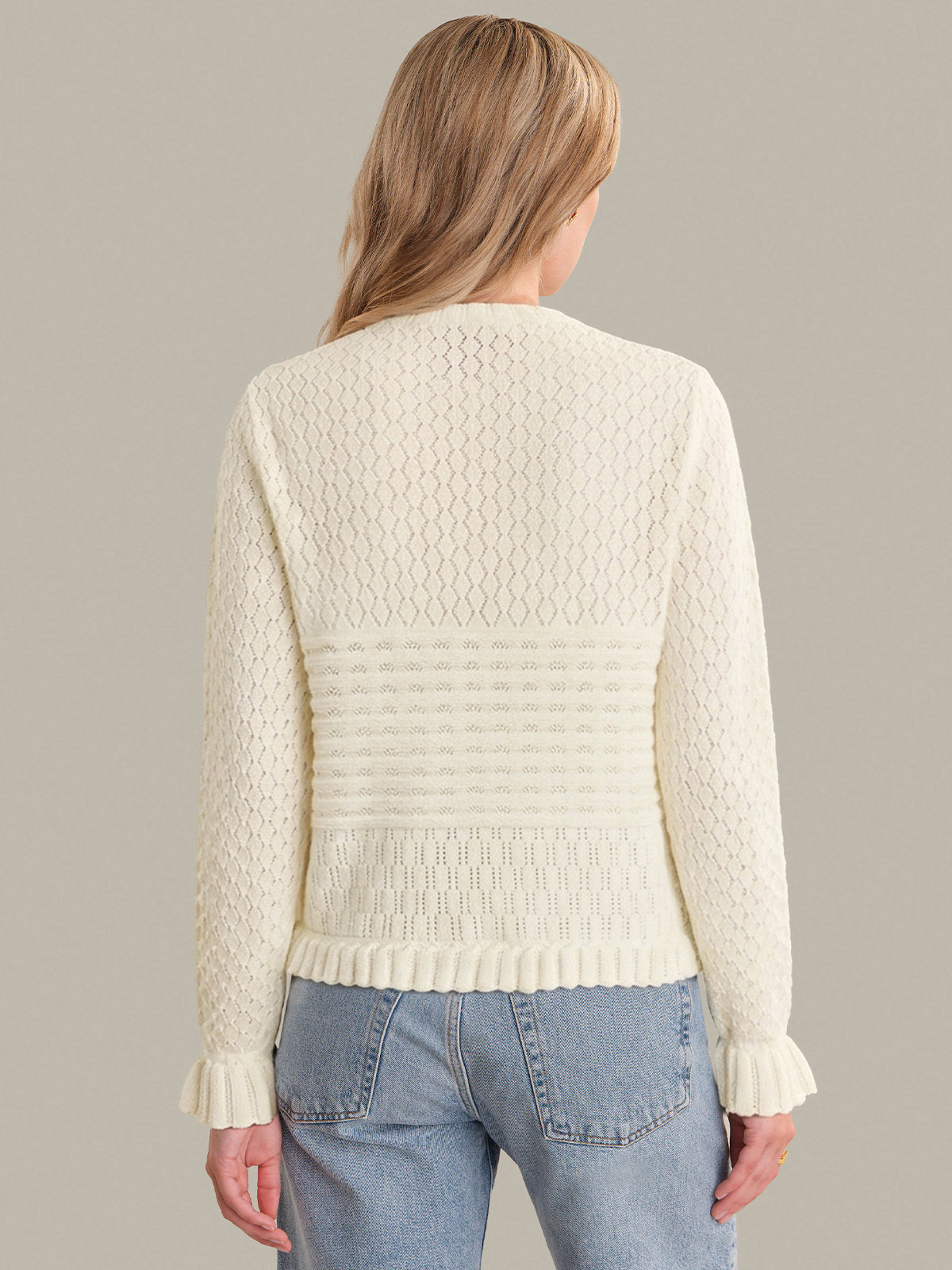 Person wearing a cream knitted sweater and blue jeans on a gray background