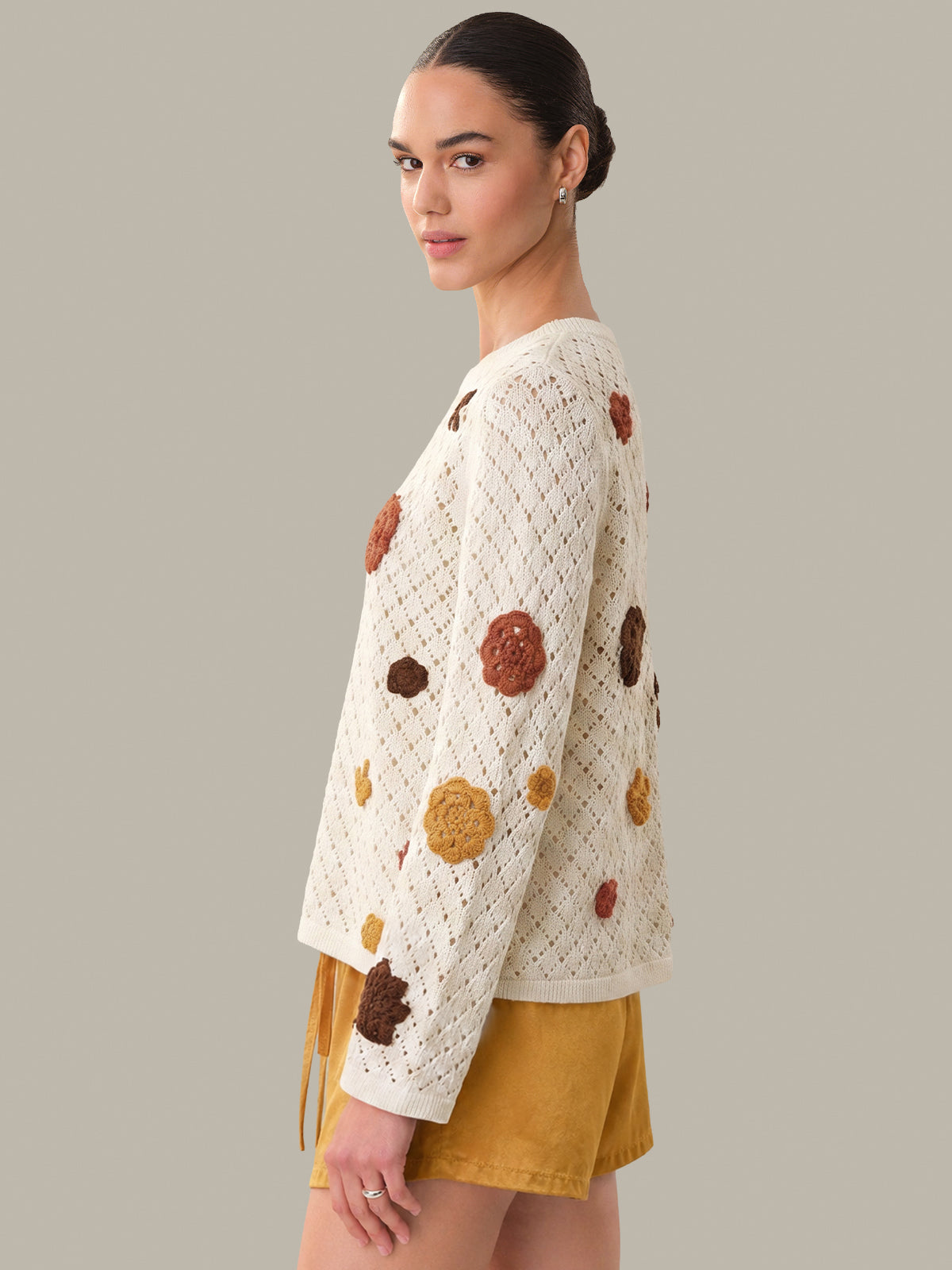 Woman wearing a white sweater with brown and orange floral patterns on a gray background