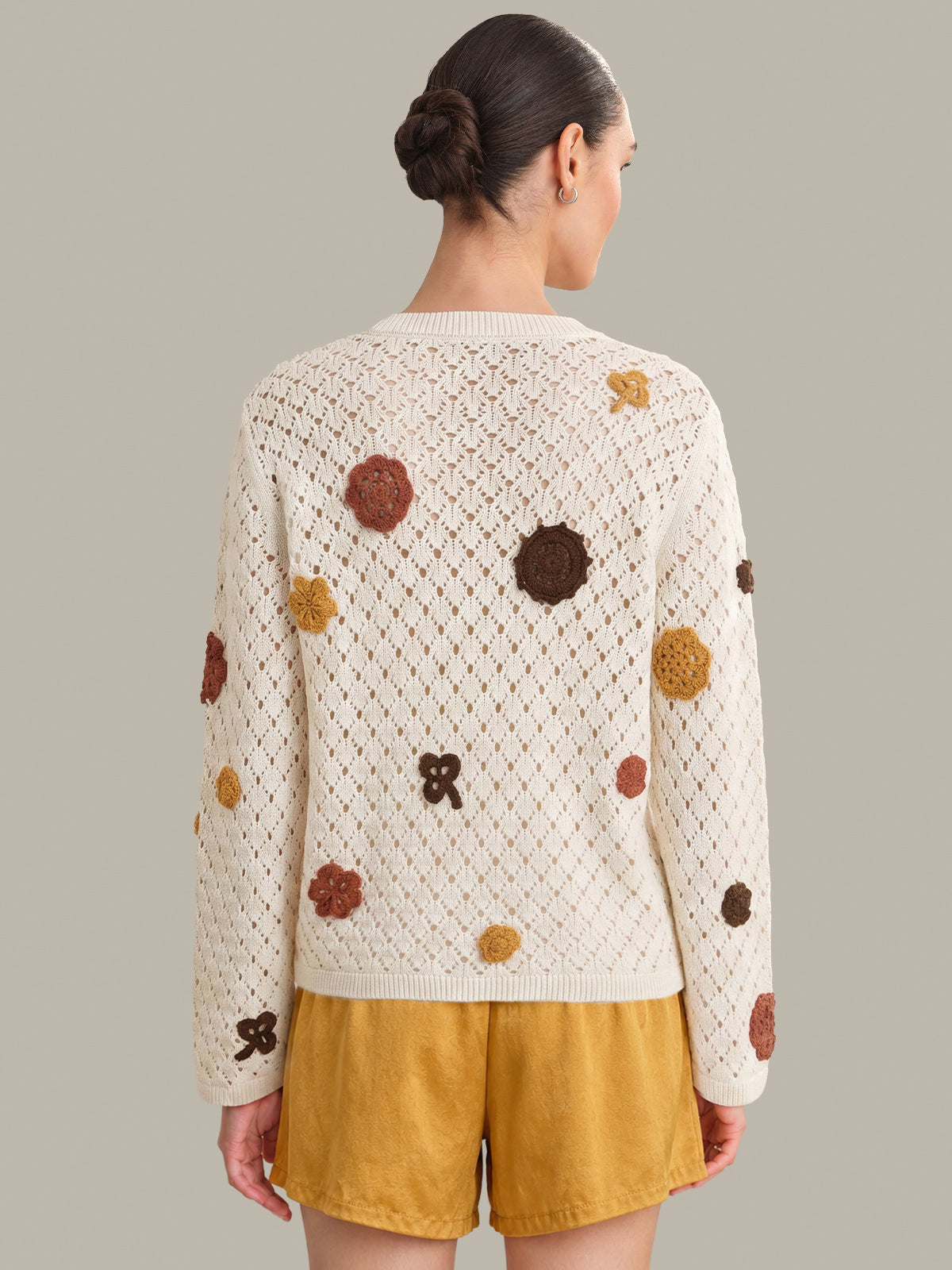 Person wearing a cream-colored cardigan with brown and yellow floral patterns on a gray background