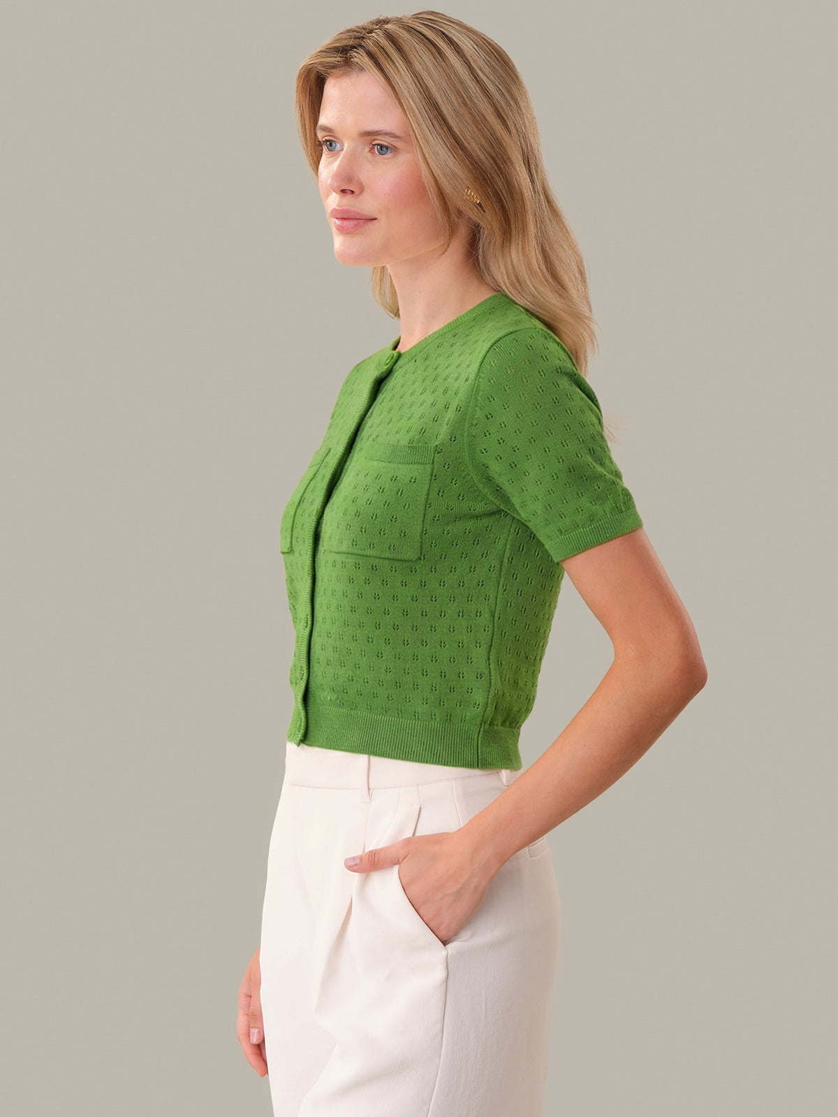 Woman wearing a green textured top and white pants against a gray background