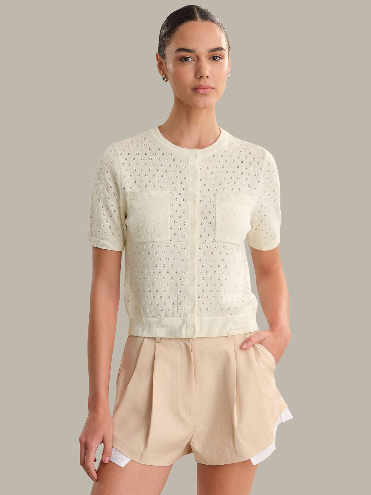 Woman wearing a light-colored short-sleeve top and shorts against a neutral background