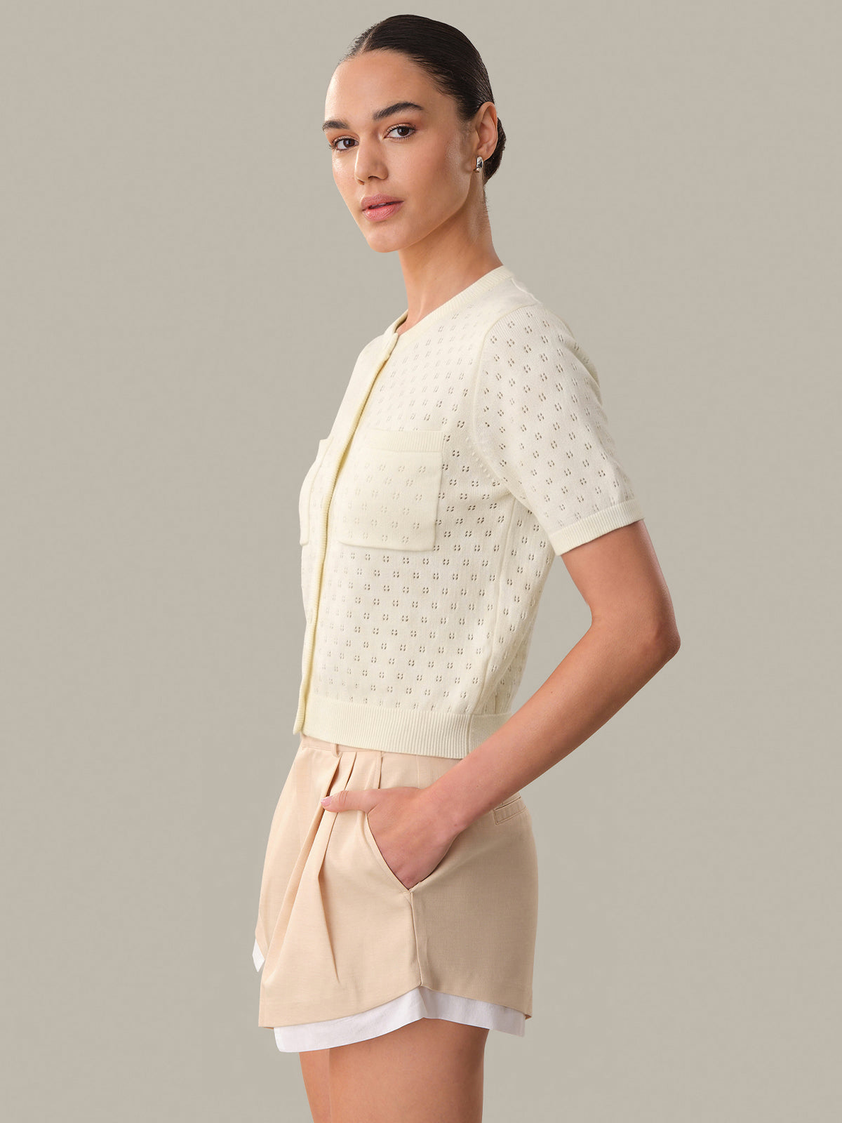 Woman wearing a light-colored outfit with a textured top and shorts on a neutral background