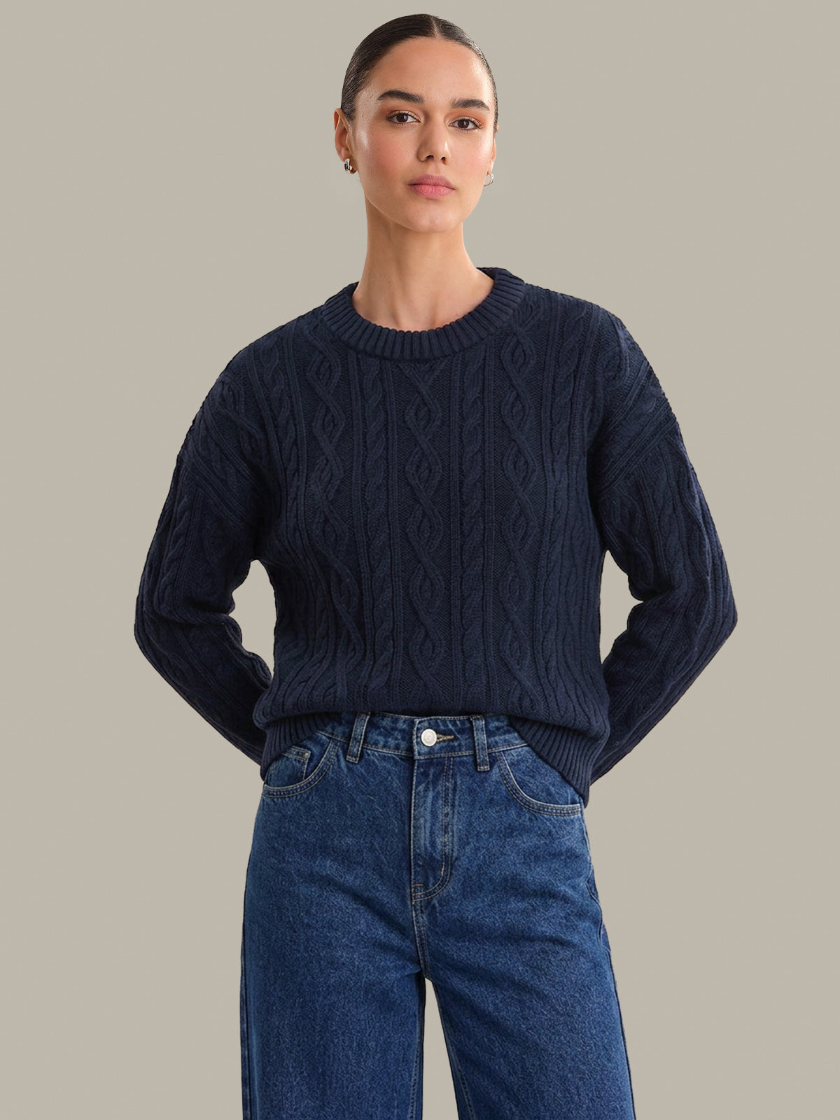Person wearing a navy blue cable knit sweater and blue jeans on a neutral background