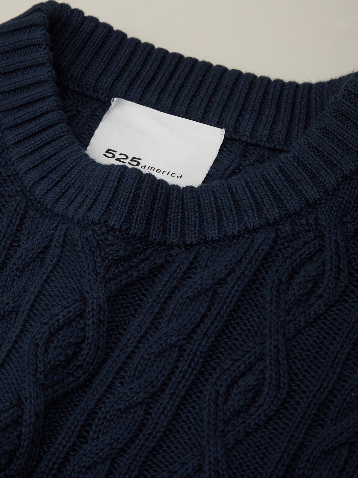 Close-up of a navy blue cable knit sweater with a brand label on the collar.