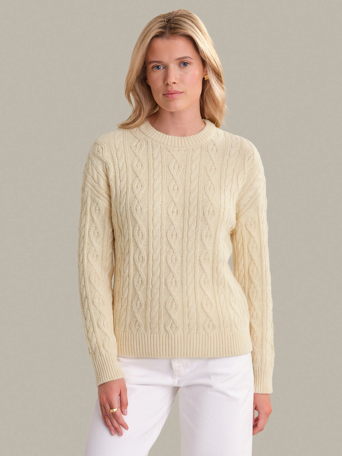 Woman wearing a beige cable knit sweater against a plain background