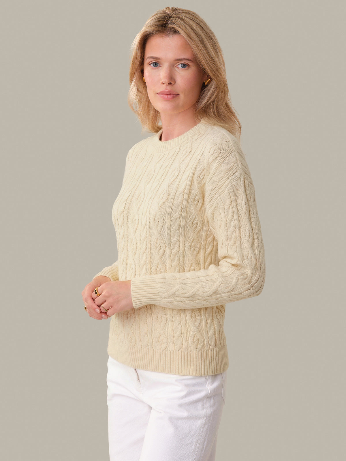 Woman wearing a cream cable knit sweater against a plain background