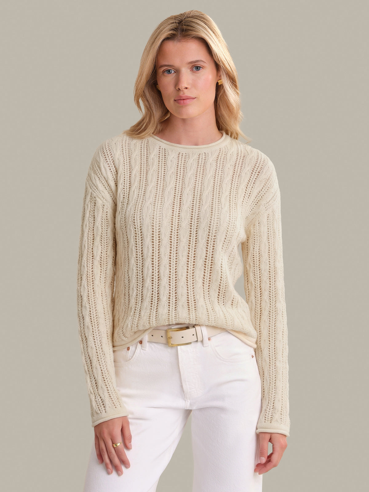 Woman wearing a cream sweater and white pants against a neutral background