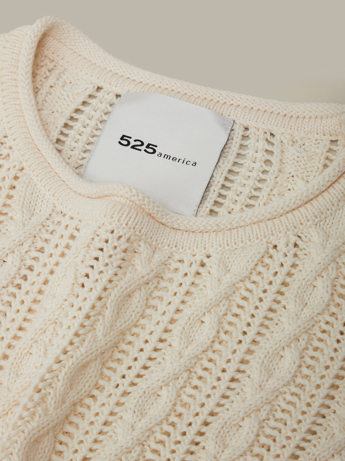 Close-up of a beige knitted sweater with a brand label on a neutral background