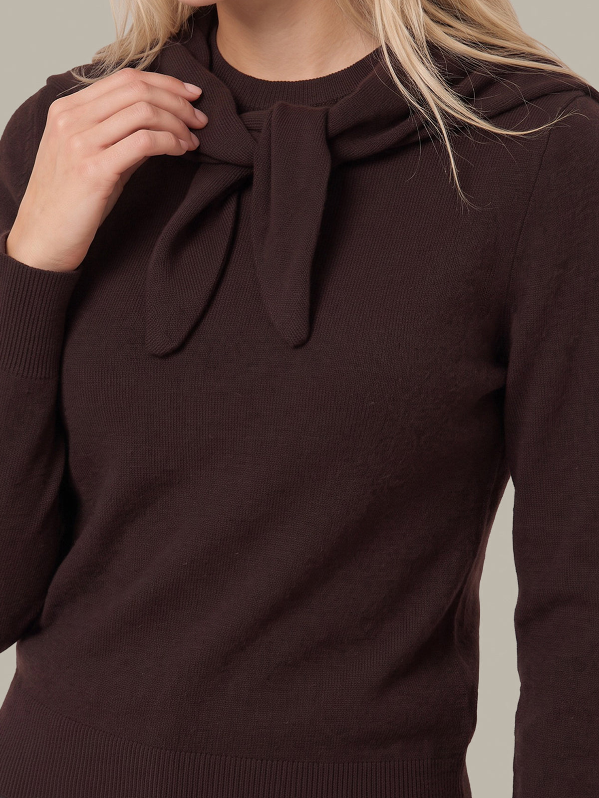 A close-up of a woman wearing a dark brown ribbed knit sweater with a large bow detail at the neckline.