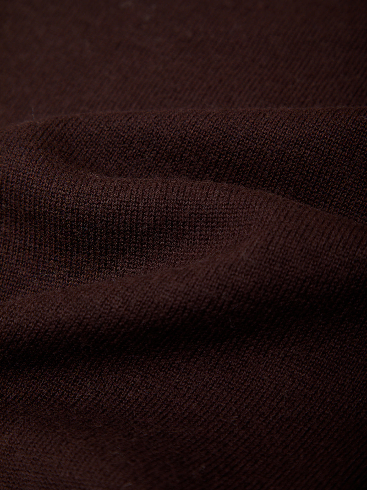 A close-up of dark brown knit fabric with soft folds showing the texture and weave.