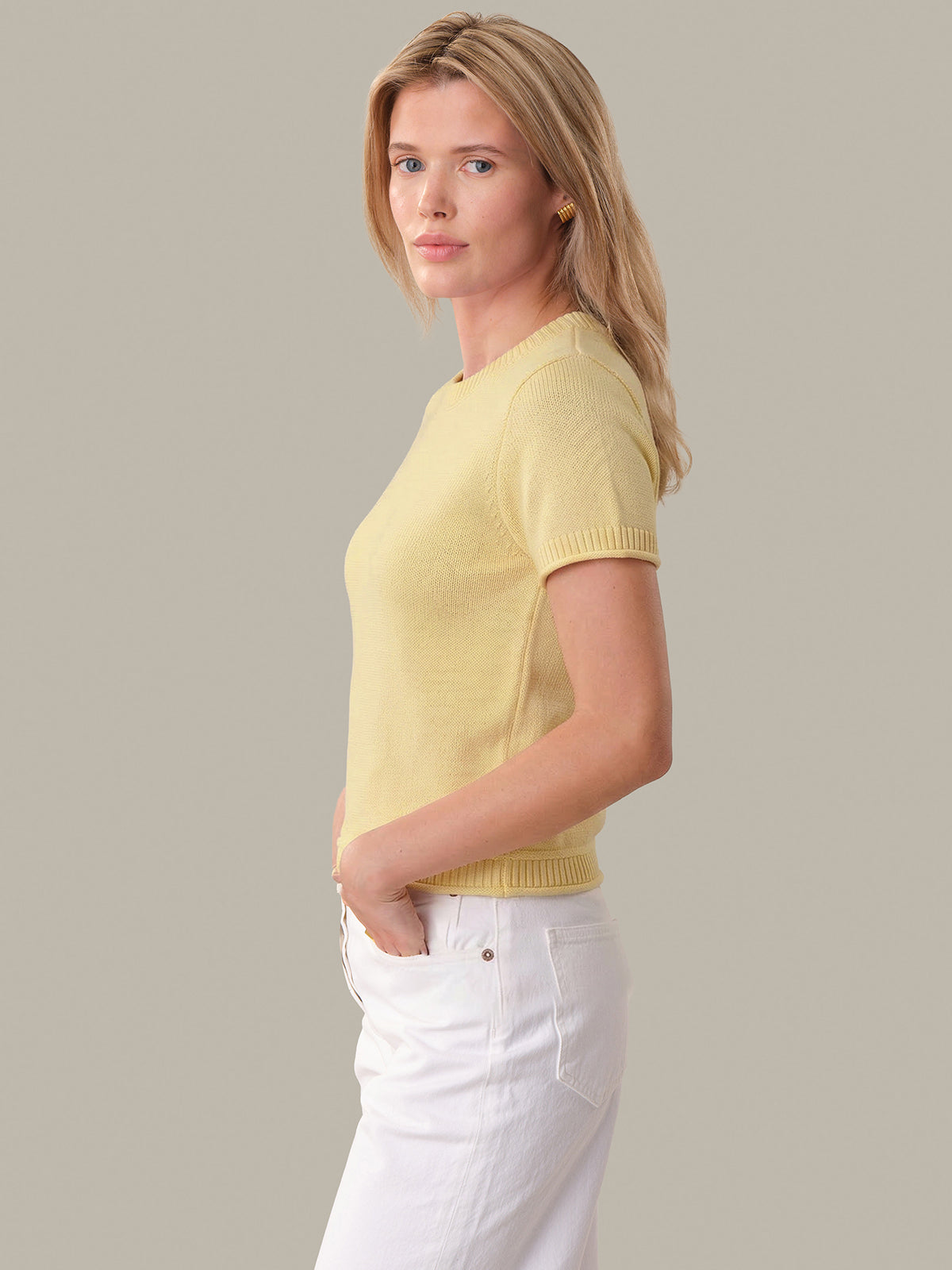 Woman wearing a yellow sweater and white pants against a plain background