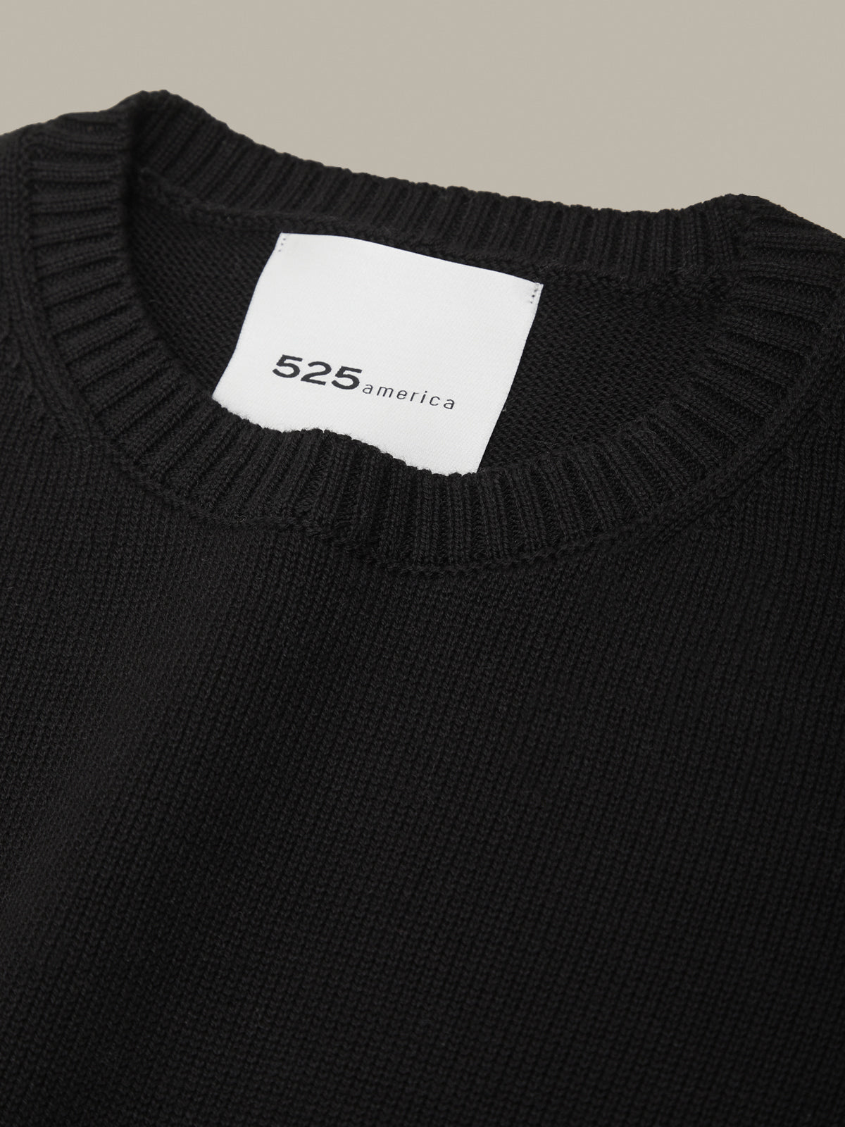Black sweater with a visible brand label on a neutral background