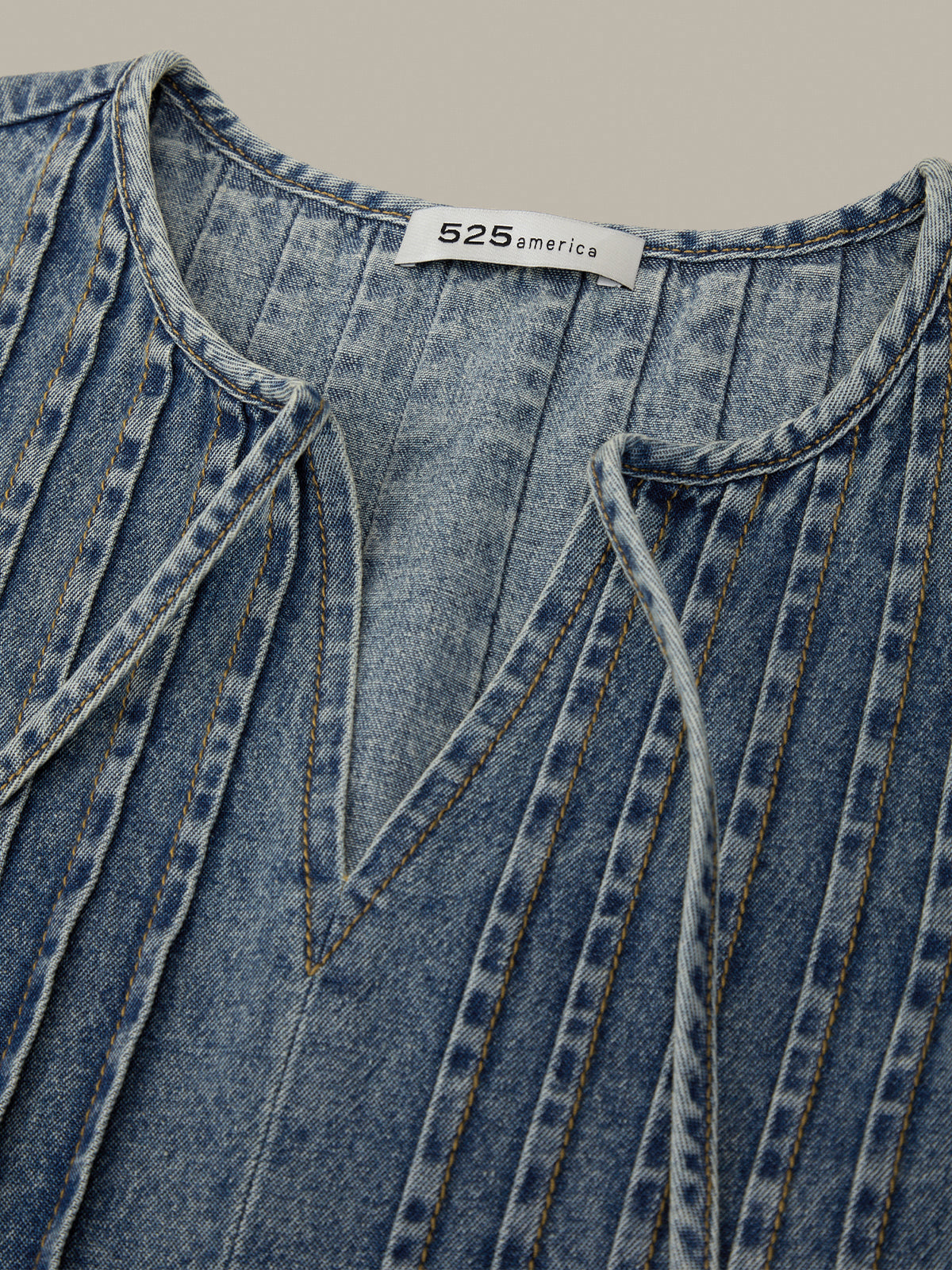 Close-up of a blue denim shirt with a brand label on a beige background