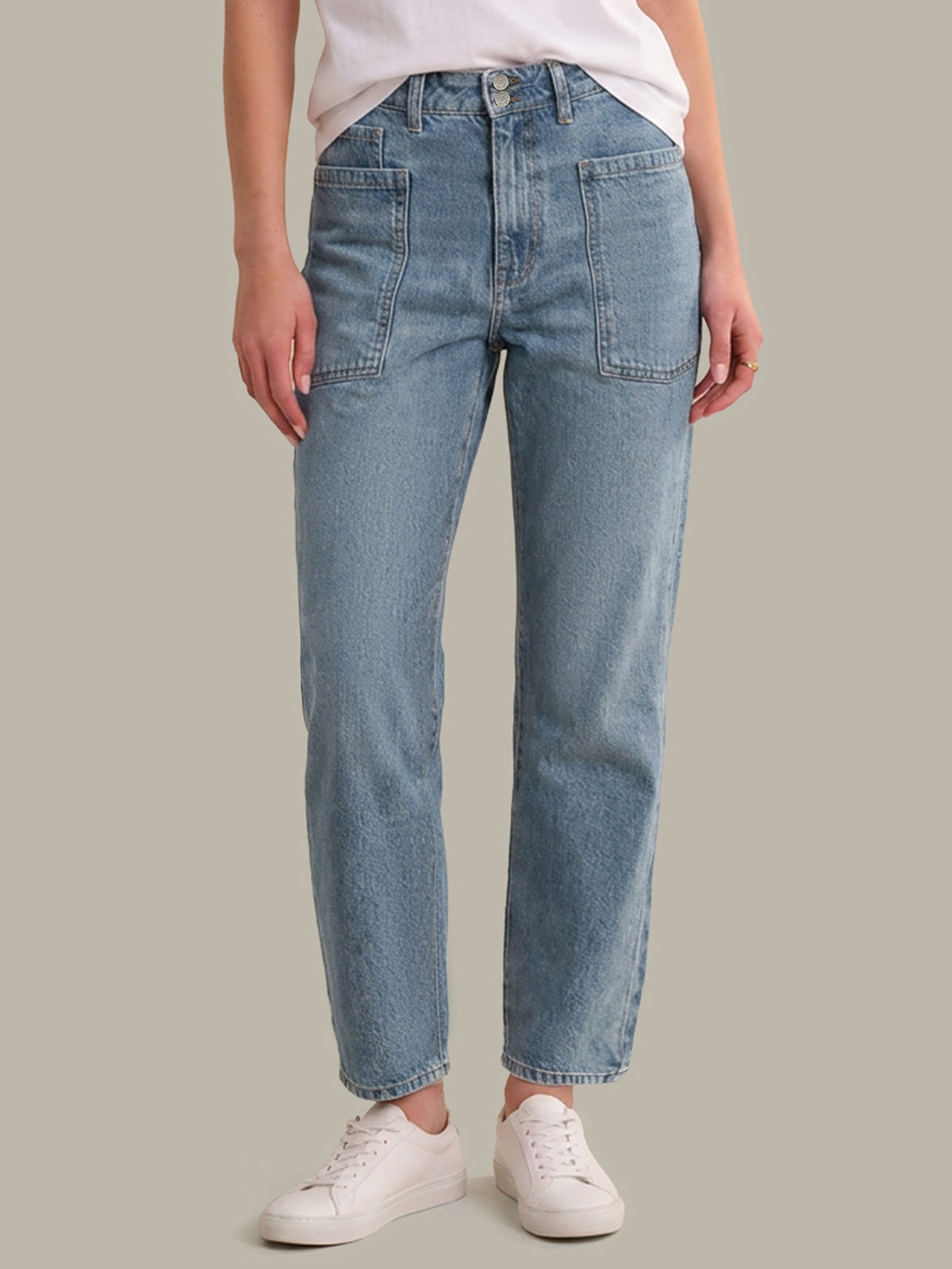 Person wearing light blue jeans and white sneakers on a neutral background