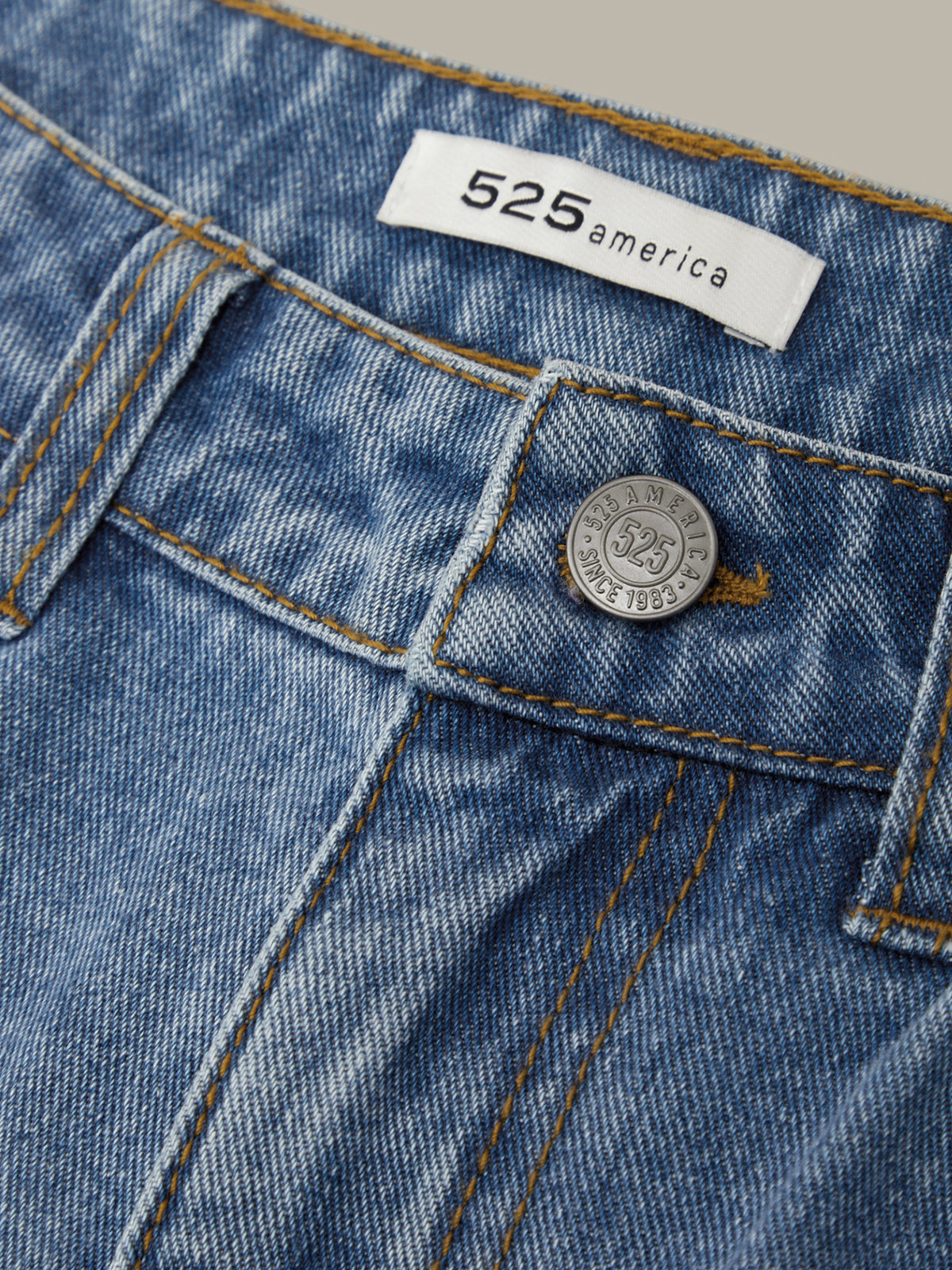 Close-up of blue denim jeans with a button and '525 America' label.