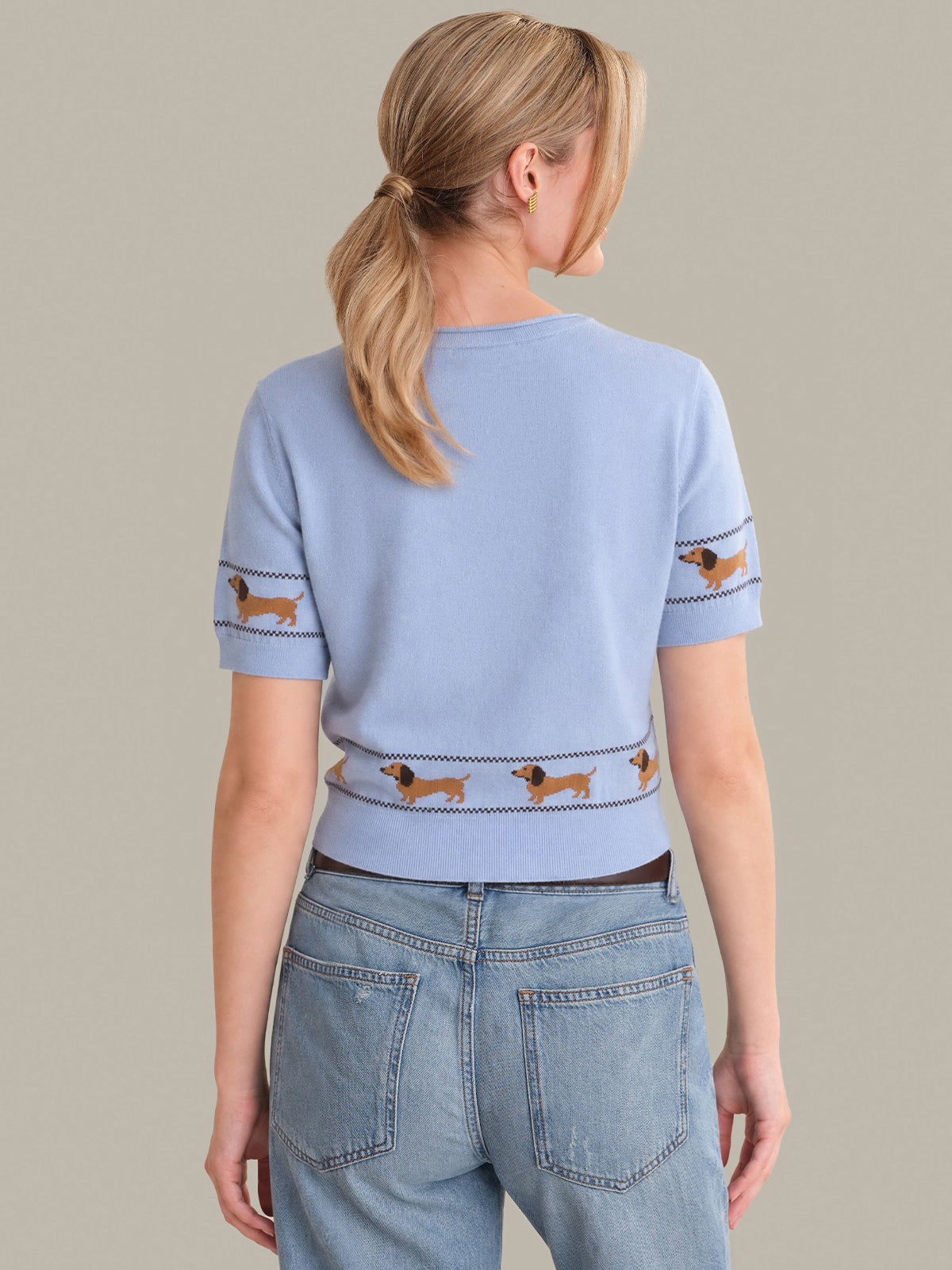 Person wearing a light blue sweater with dachshund patterns on a plain background