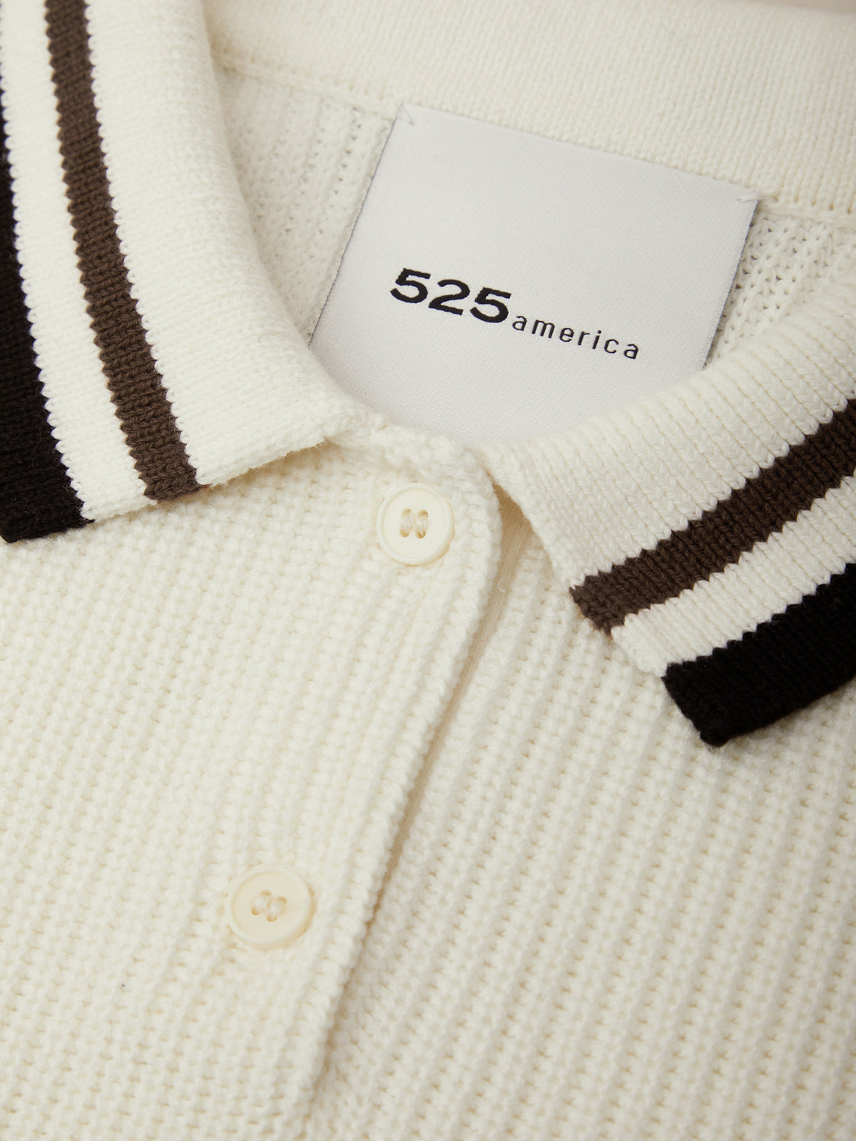 Close-up of a cream-colored polo shirt with brown stripes and a visible brand tag.