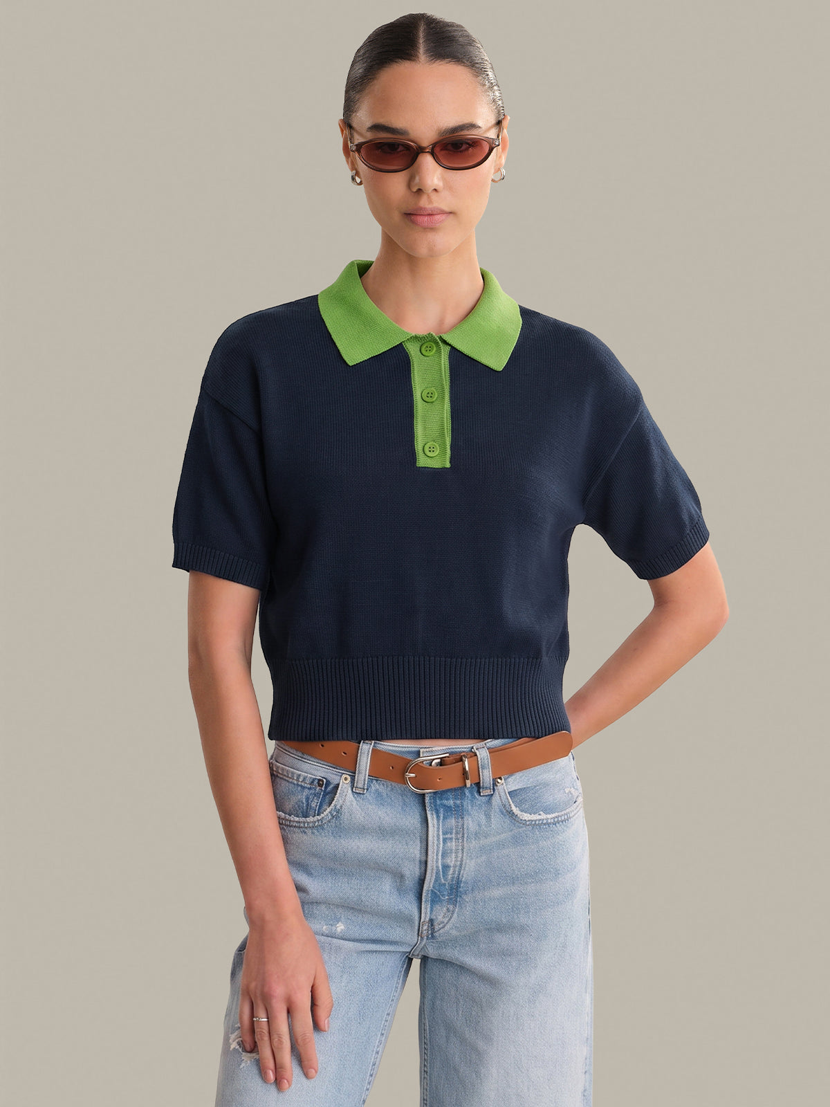 Woman wearing a navy sweater with green collar and light blue jeans on a neutral background