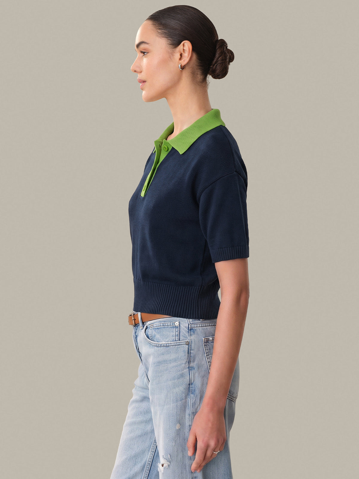 Woman wearing a navy sweater with green collar against a neutral background