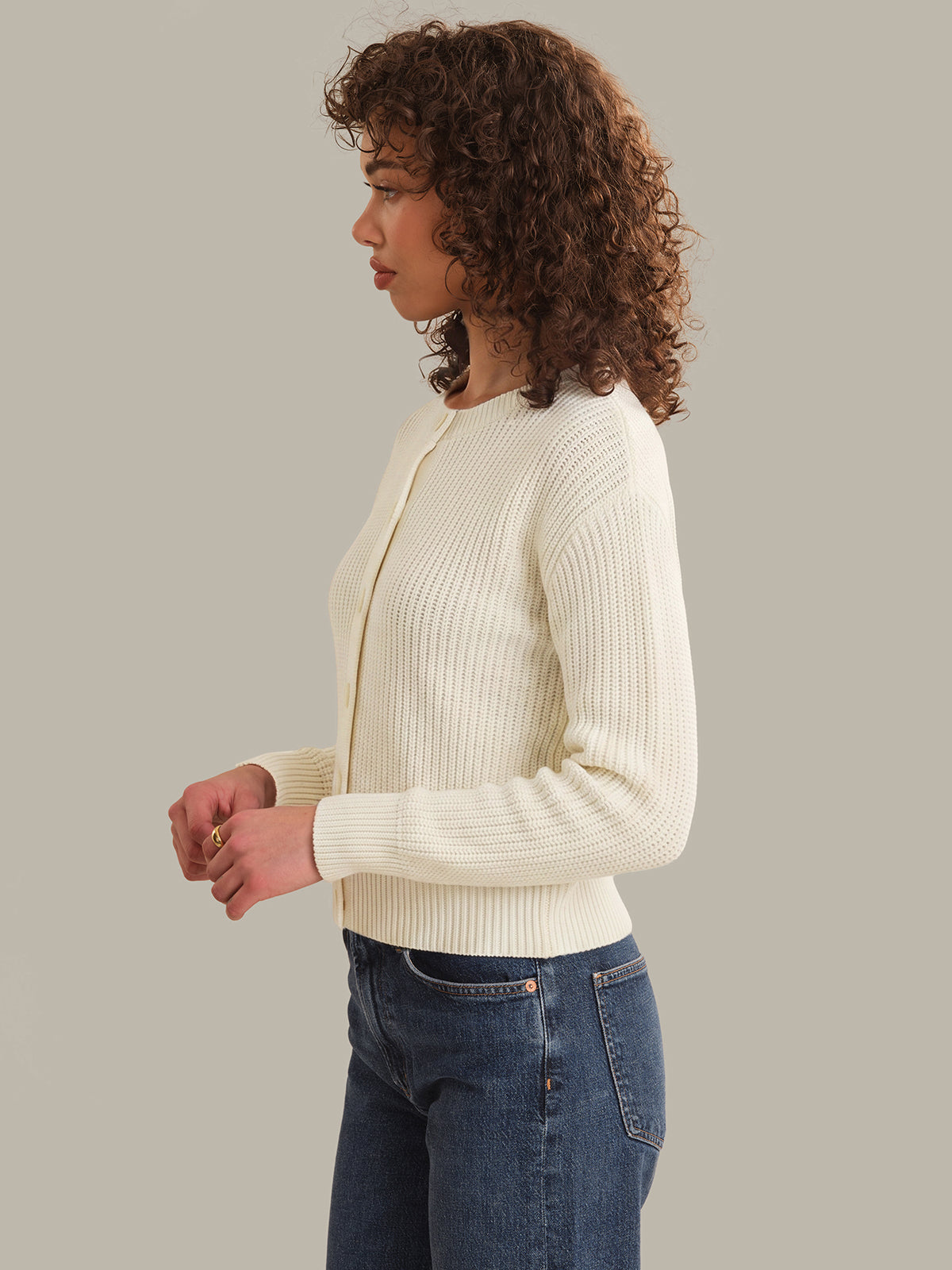 Woman wearing a cream ribbed sweater and blue jeans on a neutral background