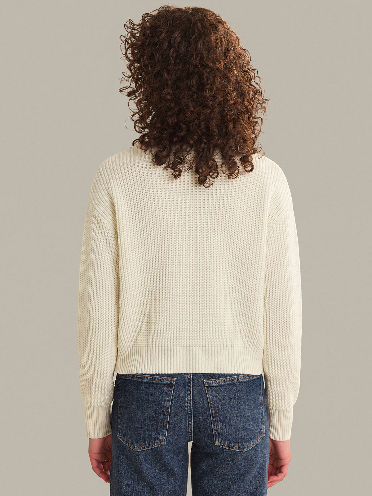 Person wearing a cream ribbed sweater and blue jeans on a plain background