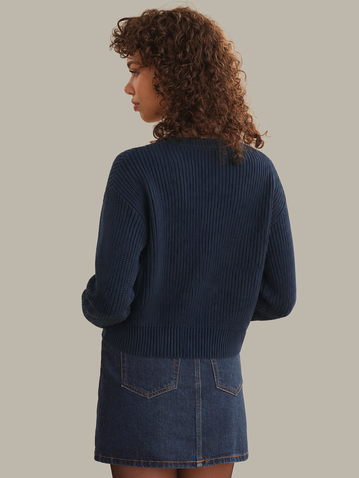 Woman wearing a navy sweater and denim skirt on a plain background