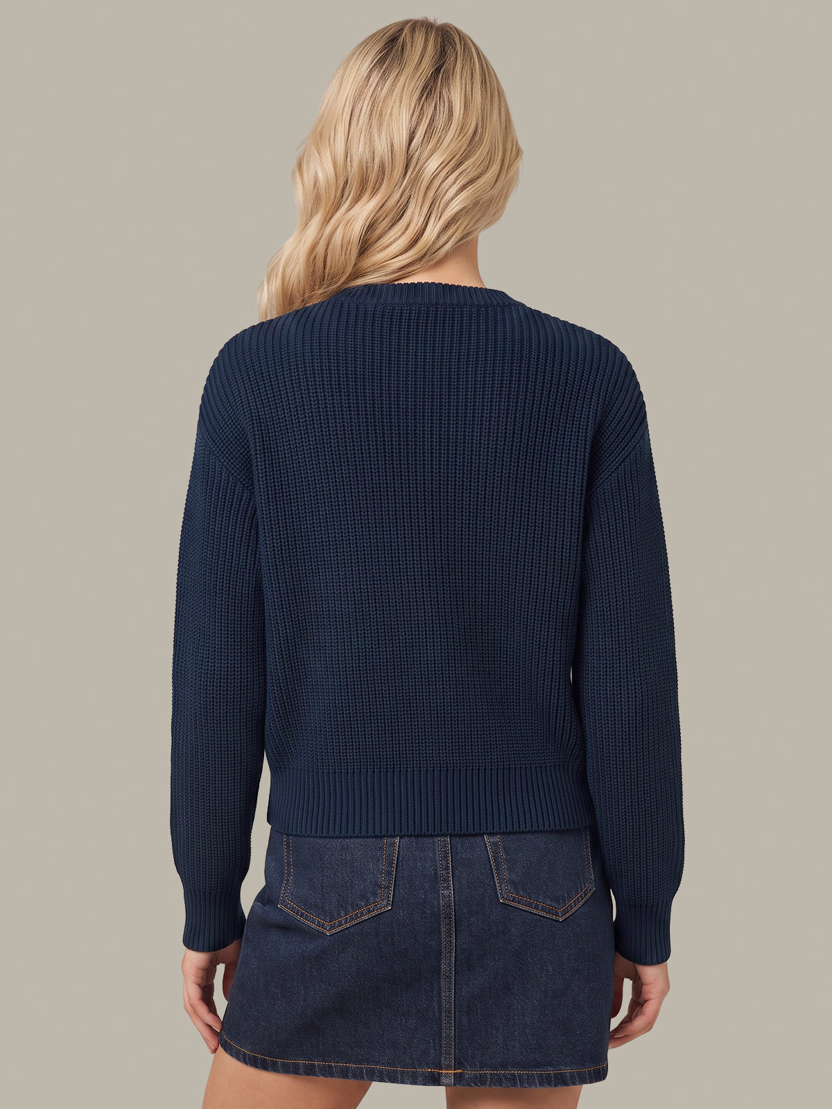 A woman shown from the back wearing a navy blue ribbed knit sweater and a dark denim mini skirt against a solid beige background.