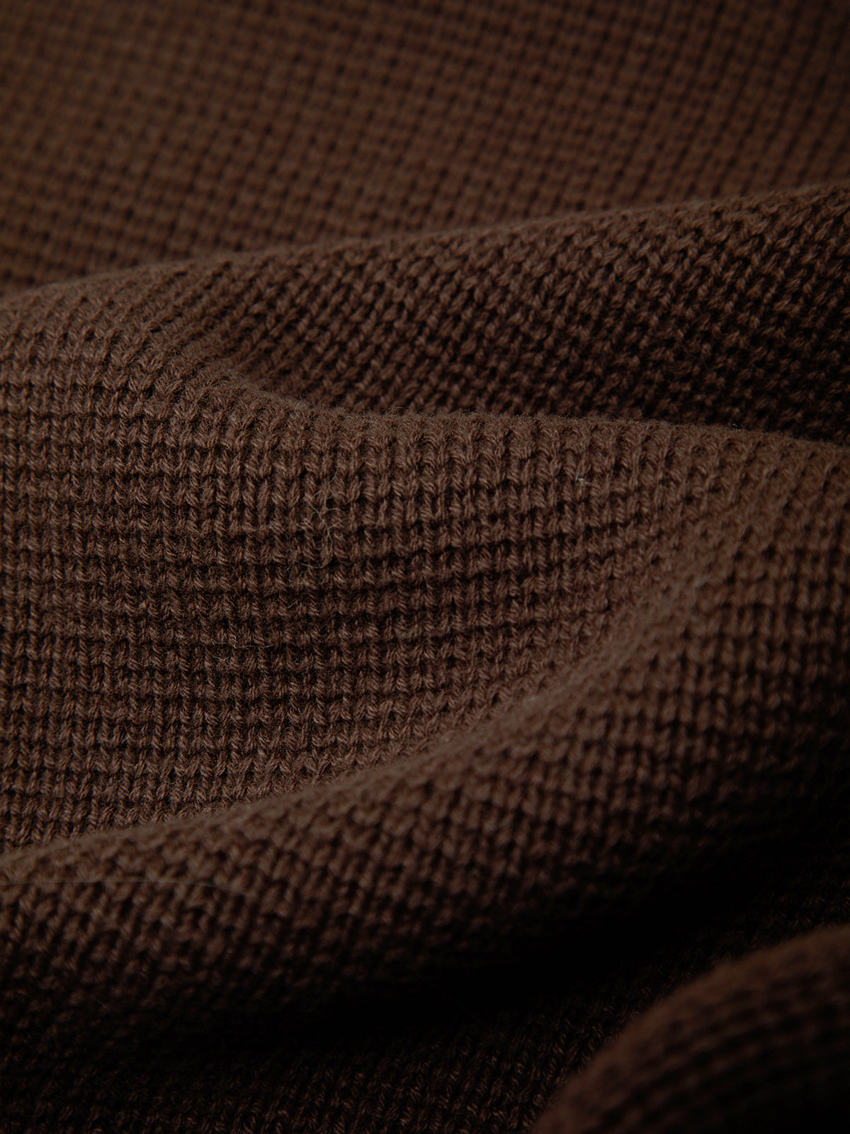 A close-up of draped brown knit fabric with a textured waffle or basketweave pattern.