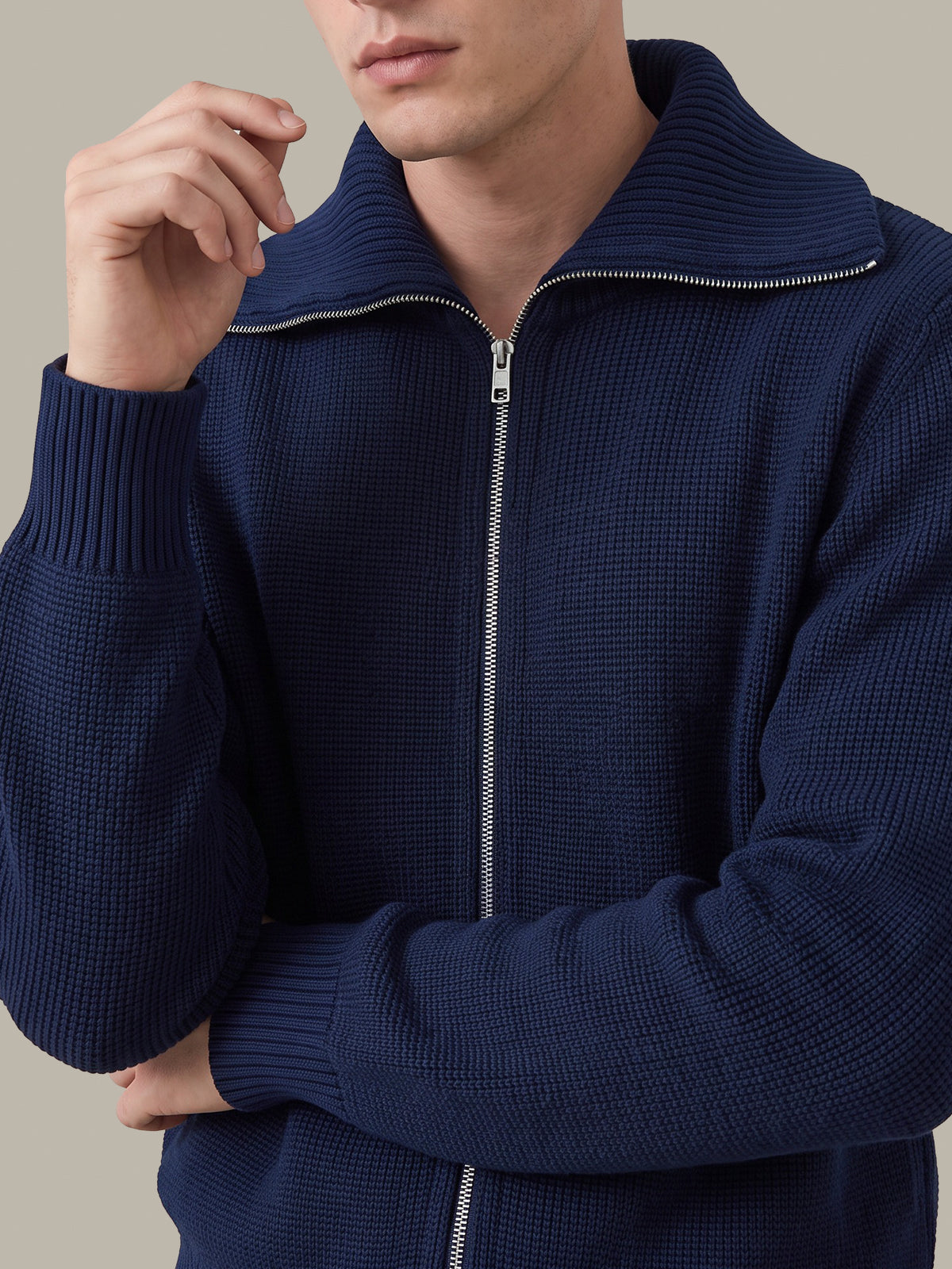 A close-up of a man wearing a navy blue waffle-knit zip-up sweater with a ribbed mock neck and silver zipper.