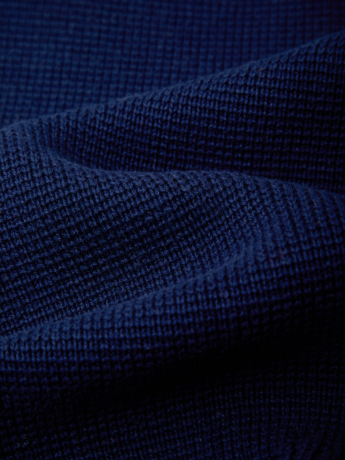 A close-up of dark navy blue textured fabric with a fine ribbed or waffle-like weave, shown in soft folds.