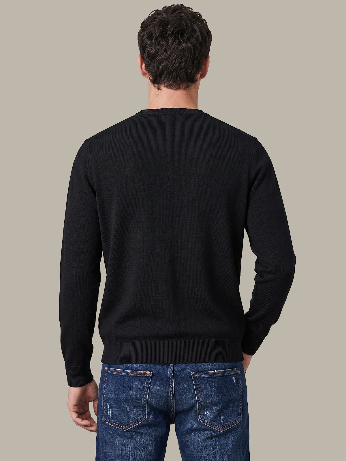 A man viewed from behind wearing a black long-sleeve crewneck sweater and blue jeans, set against a solid light gray background.
