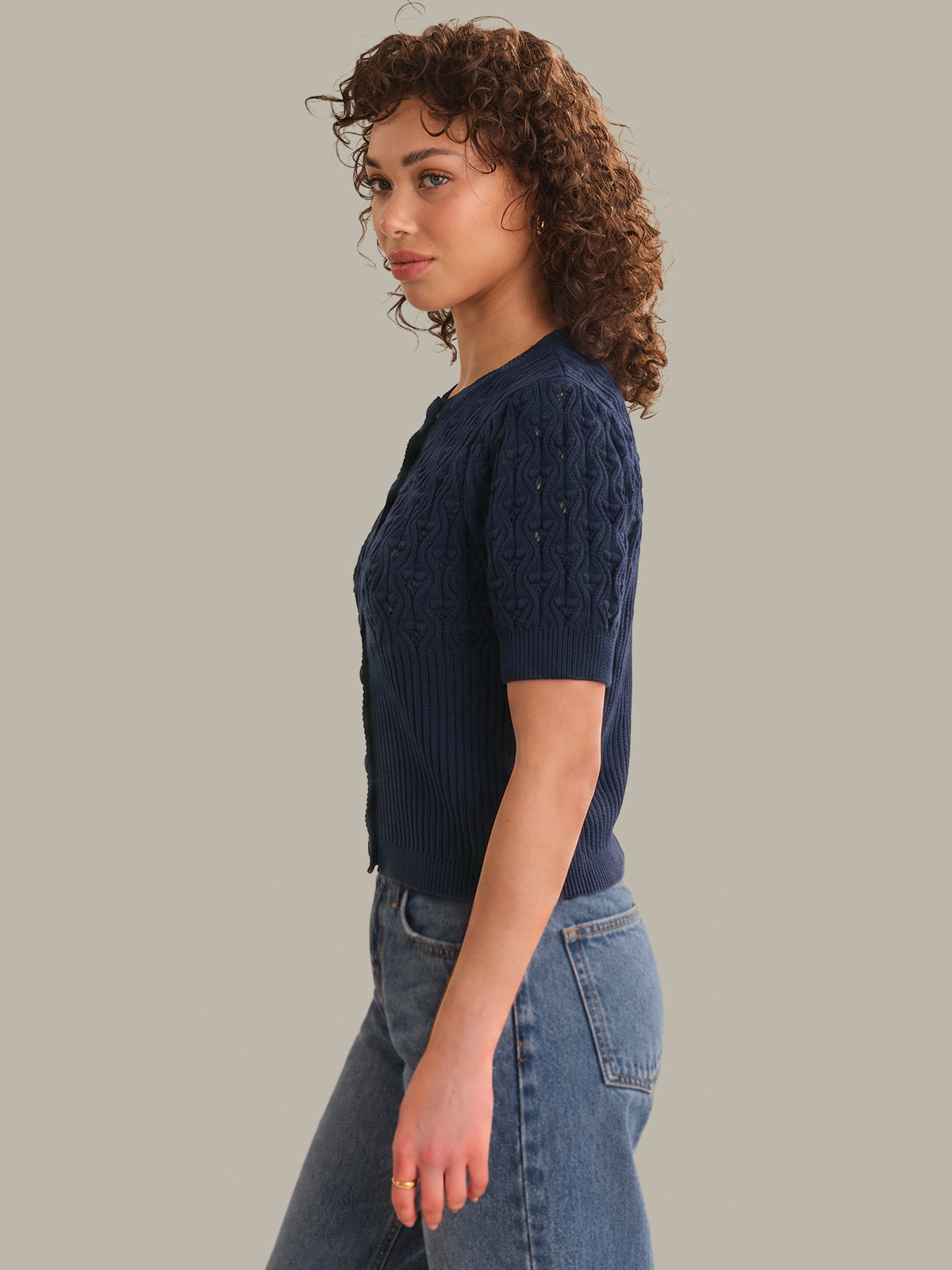 Woman wearing a navy blue knitted top and jeans on a gray background