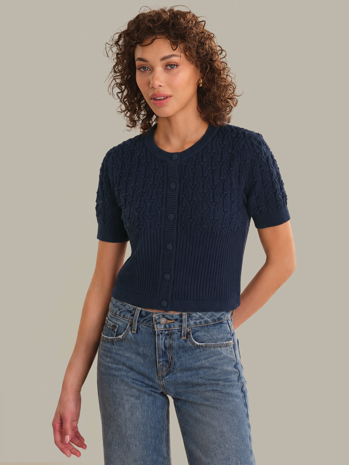 Woman wearing a navy blue knitted short-sleeve cardigan and jeans on a beige background