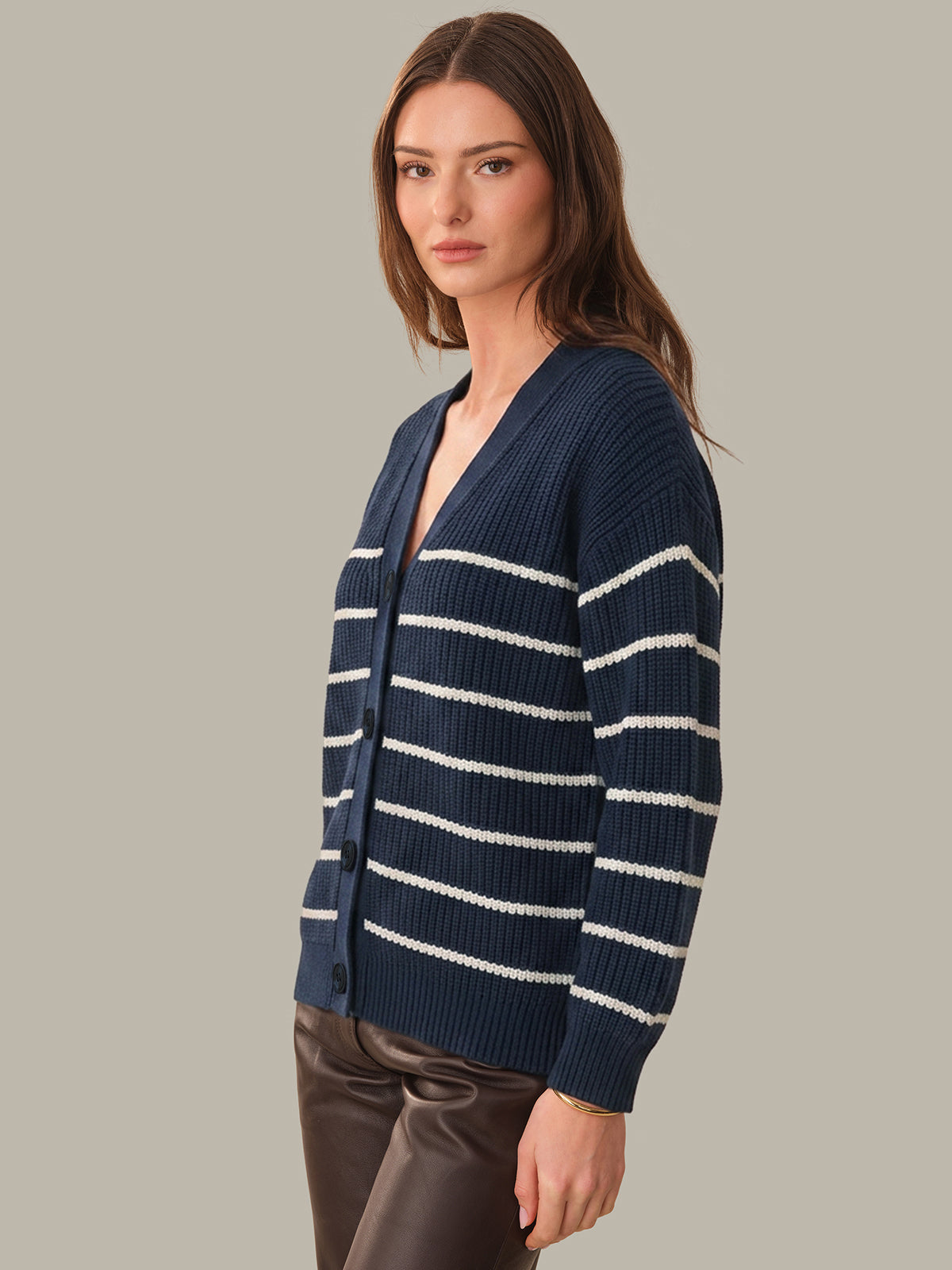 Woman wearing a navy blue cardigan with white stripes on a gray background