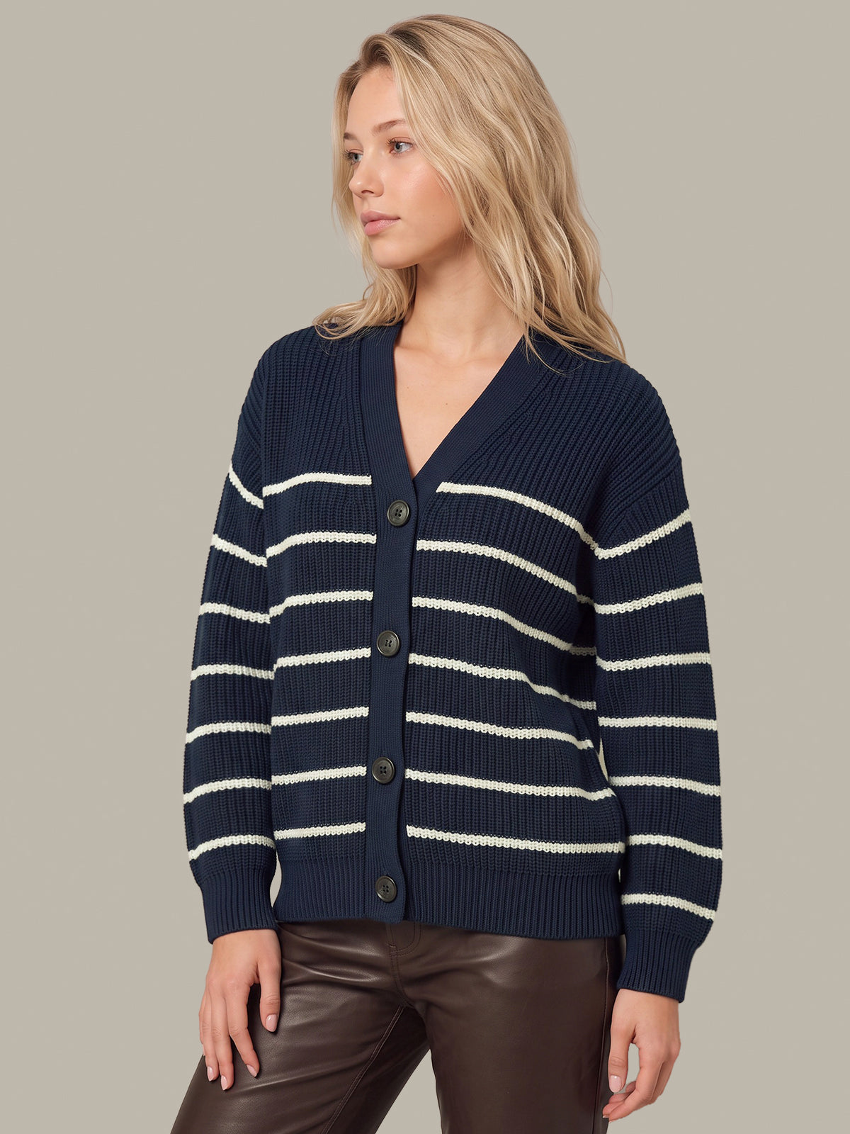 A woman wearing a navy blue ribbed cardigan with horizontal cream stripes and dark buttons, paired with dark brown pants, against a solid taupe background.