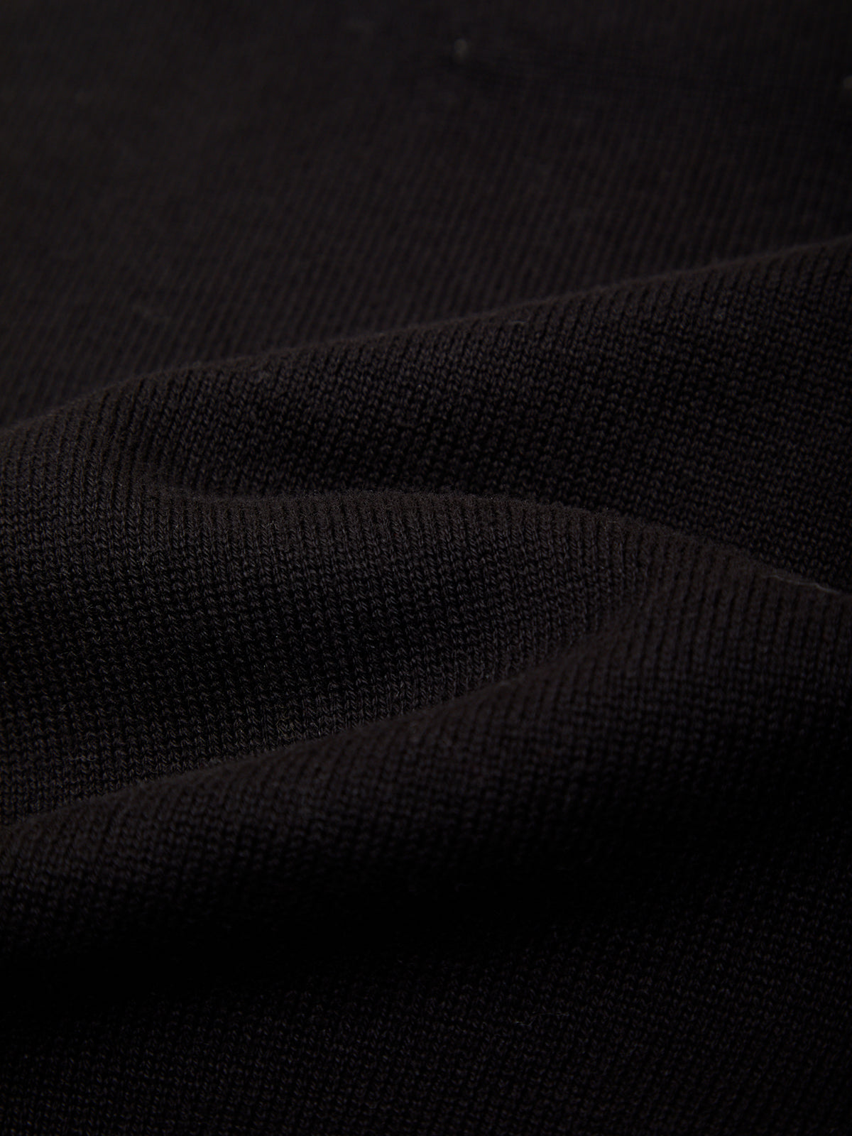 A close-up of black ribbed knit fabric with soft folds showing the texture and weave.