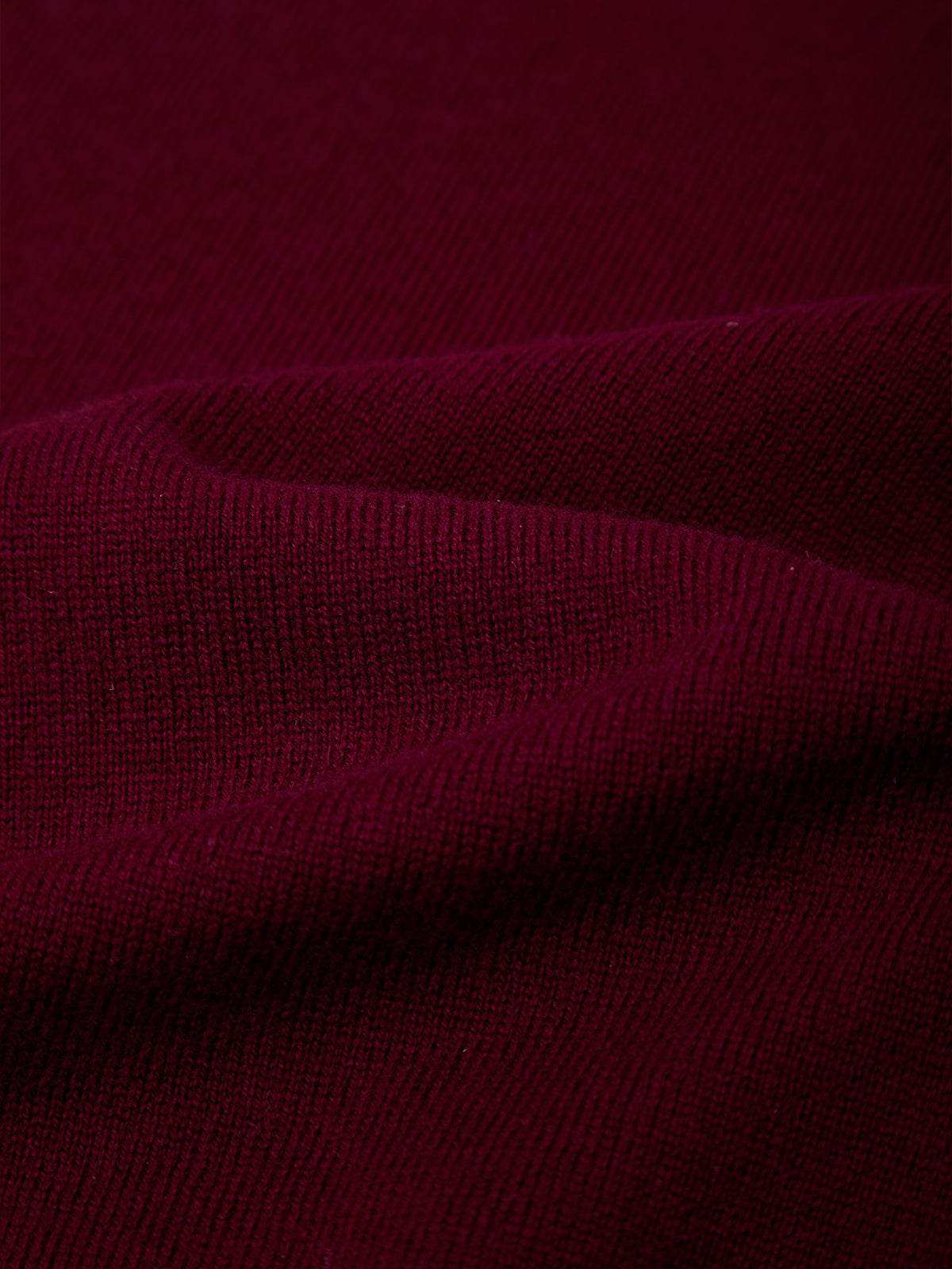 A close-up of dark burgundy knit fabric with soft folds showing the ribbed texture.