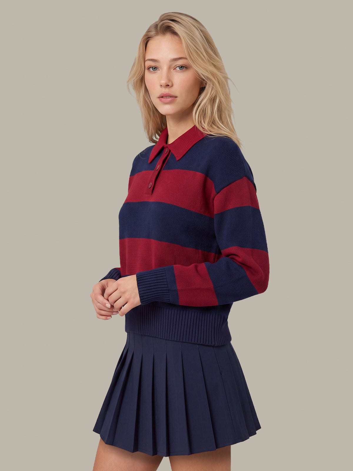 A blonde model wearing a navy and red striped knit polo sweater with a pleated navy mini skirt, posed against a solid beige background.