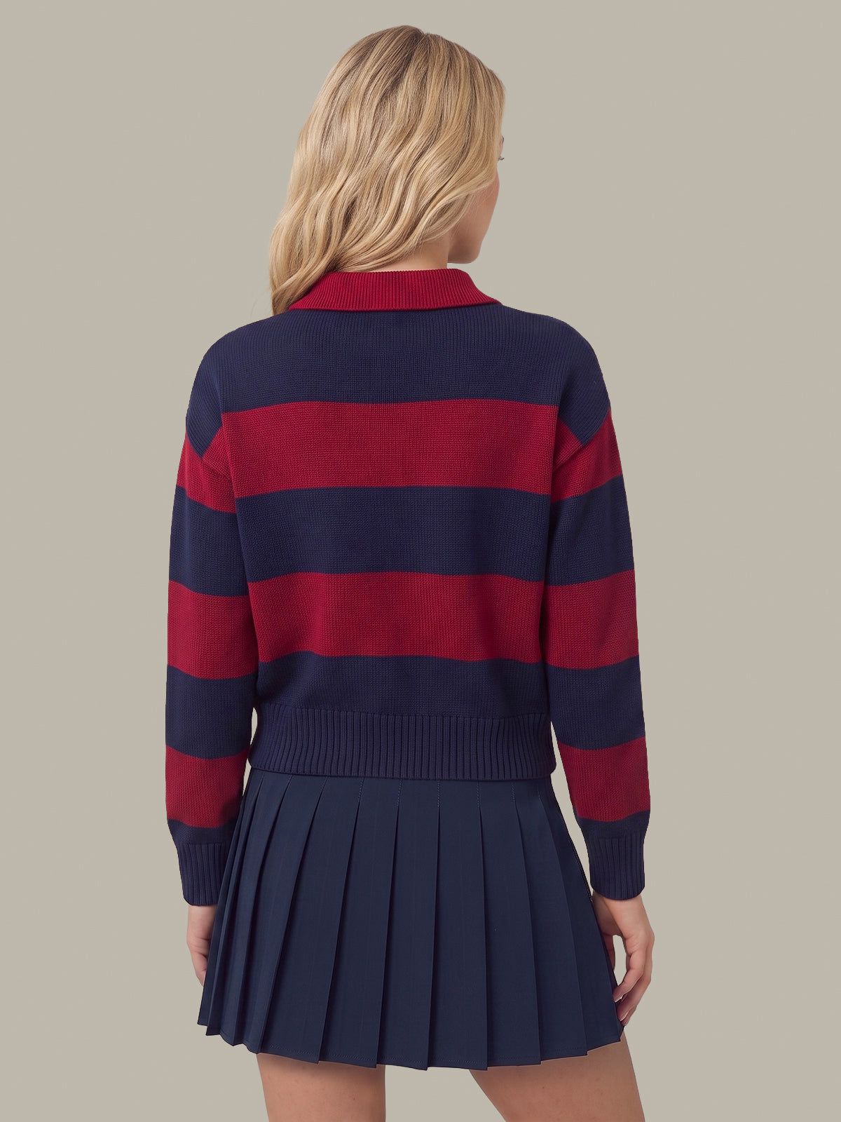A woman shown from the back wearing a navy and red horizontally striped knit sweater with a pleated navy mini skirt, against a solid beige background.