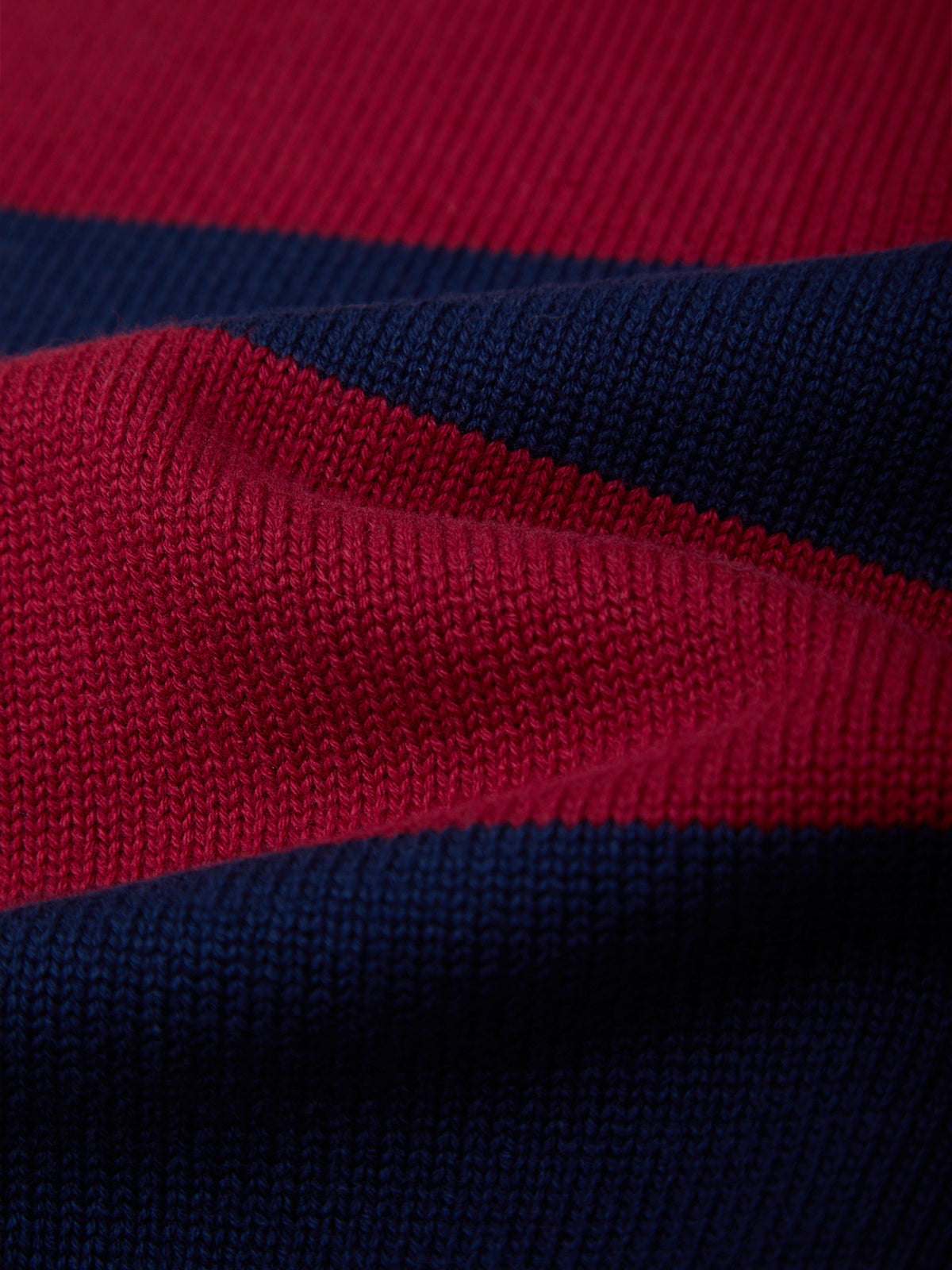 Close-up of a knitted fabric with alternating horizontal stripes of deep red and dark navy blue.