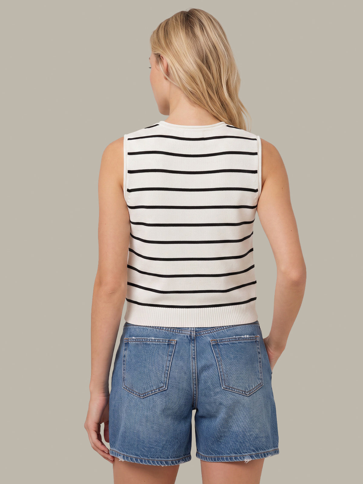 A woman shown from the back wearing a sleeveless knit top with horizontal black stripes on an off-white background, paired with blue denim shorts, against a solid taupe background.