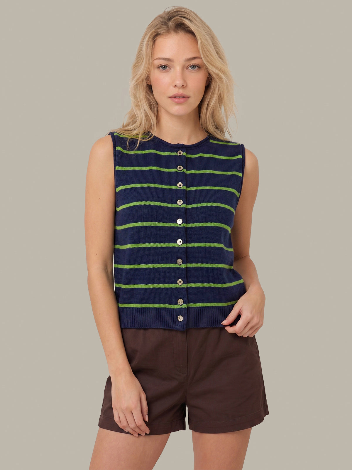 A woman modeling a sleeveless knit top with navy, green, and lime stripes, paired with brown shorts, against a solid gray background.